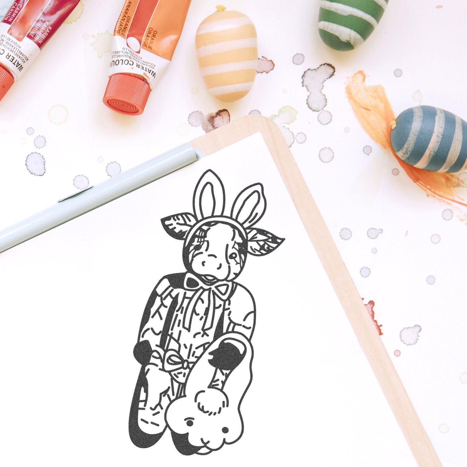 Watercolor paint tubes and painted Easter eggs surrounding a cute bunny illustration in a sketchbook.