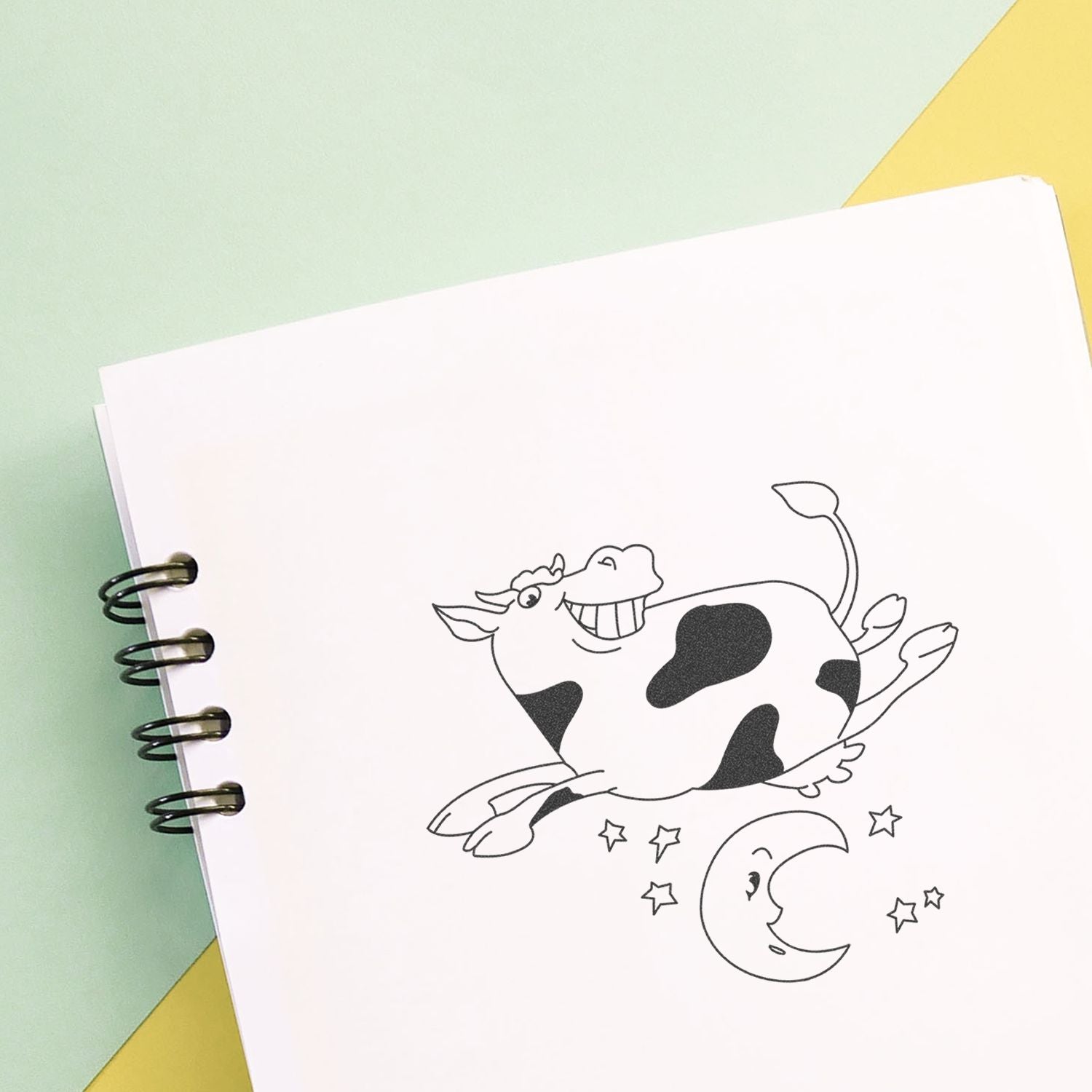 Spiral notebook with cute cow and moon illustration on pastel background, black and white coloring page design.