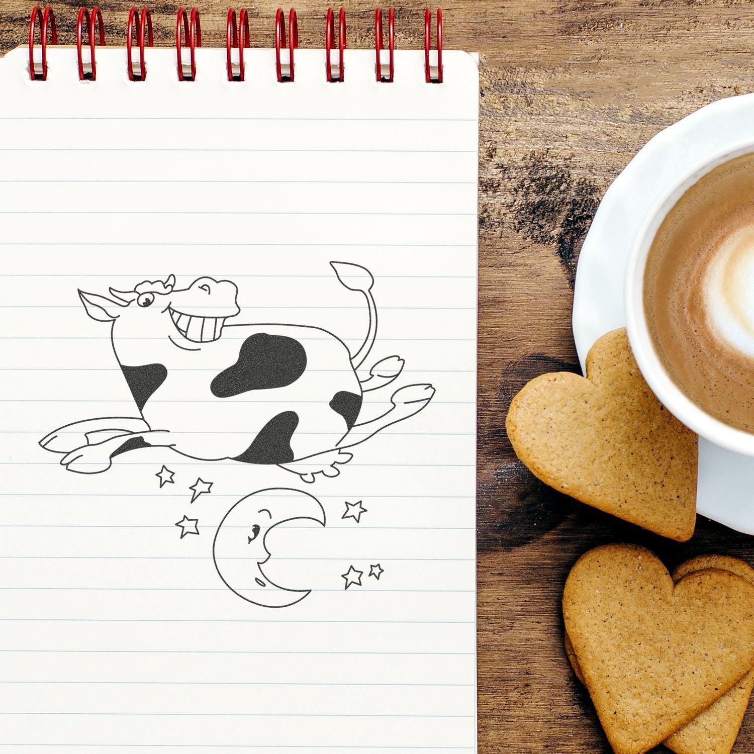 Notebook with cute cow doodle beside coffee cup and heart-shaped cookies on rustic wooden table