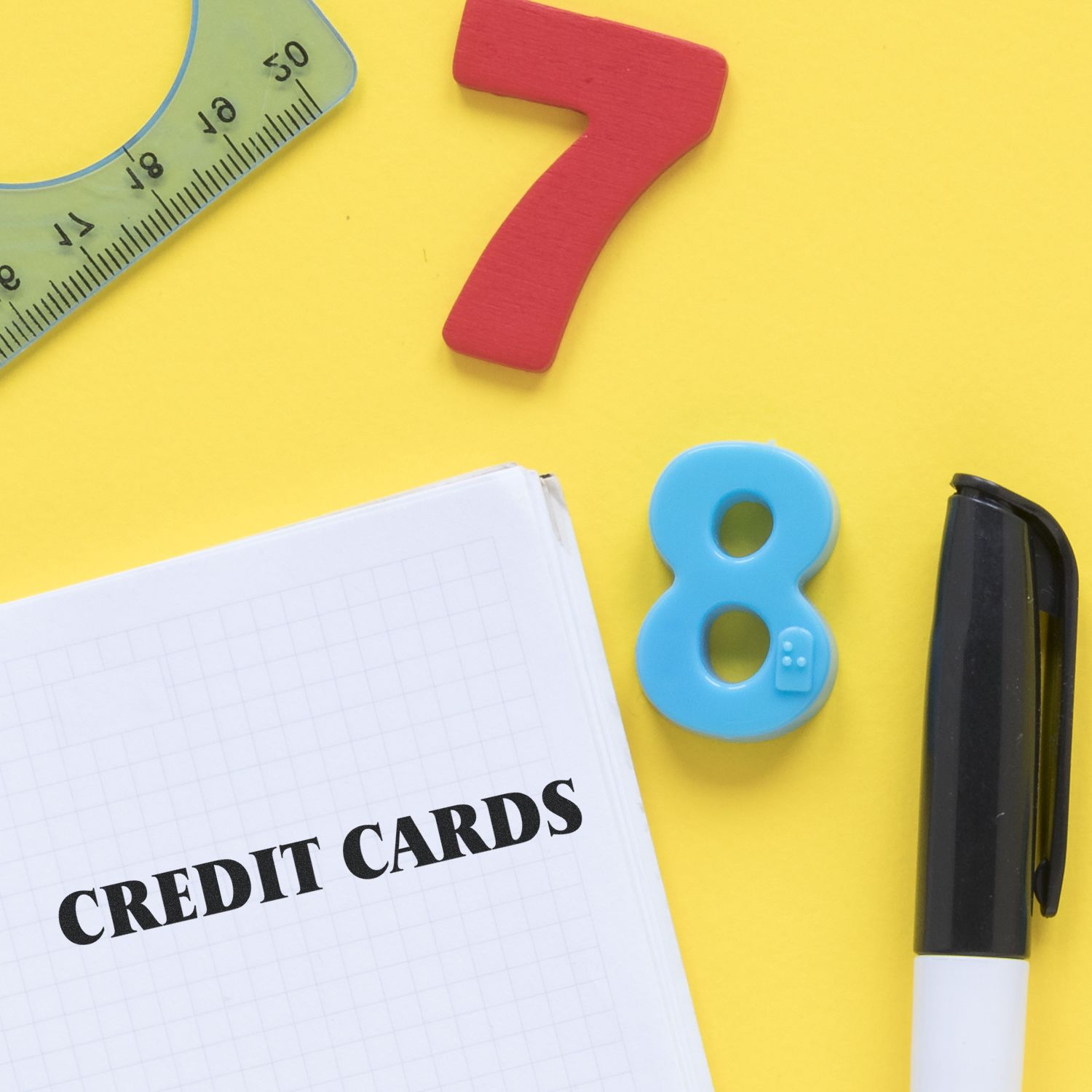 Credit cards notebook with colorful number blocks, ruler, and marker on yellow background for finance and math concept.