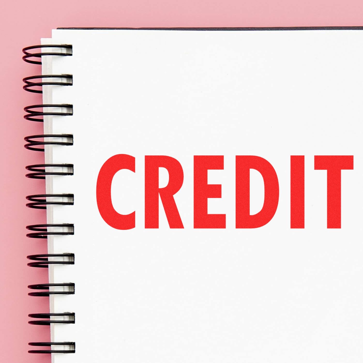 Notebook with red CREDIT text on white page, spiral binding, and pink background, representing finance and credit management.