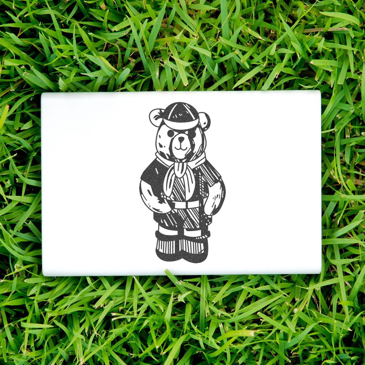 White laptop with cute bear illustration on green grass, outdoor product display.