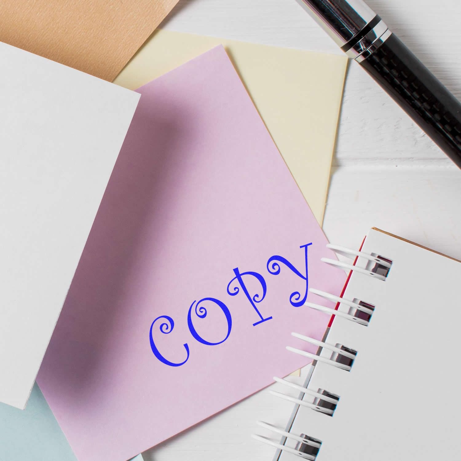 Pastel stationery notebooks with pen and notebook labeled copy on a white desk.