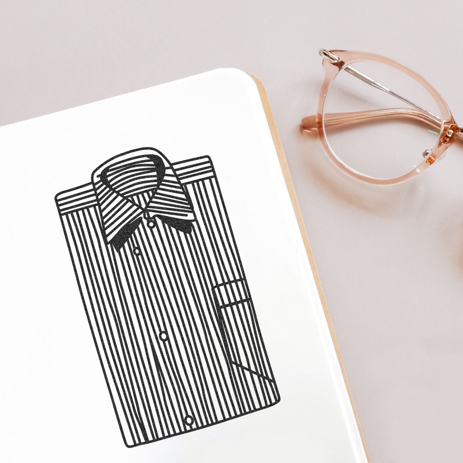 Minimalist notebook with black striped shirt illustration and pink eyeglasses on a soft pastel background.