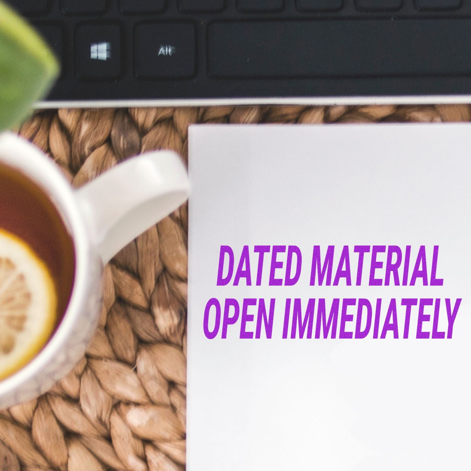 Coffee cup beside laptop and DATED MATERIAL OPEN IMMEDIATELY notice on desk office workspace