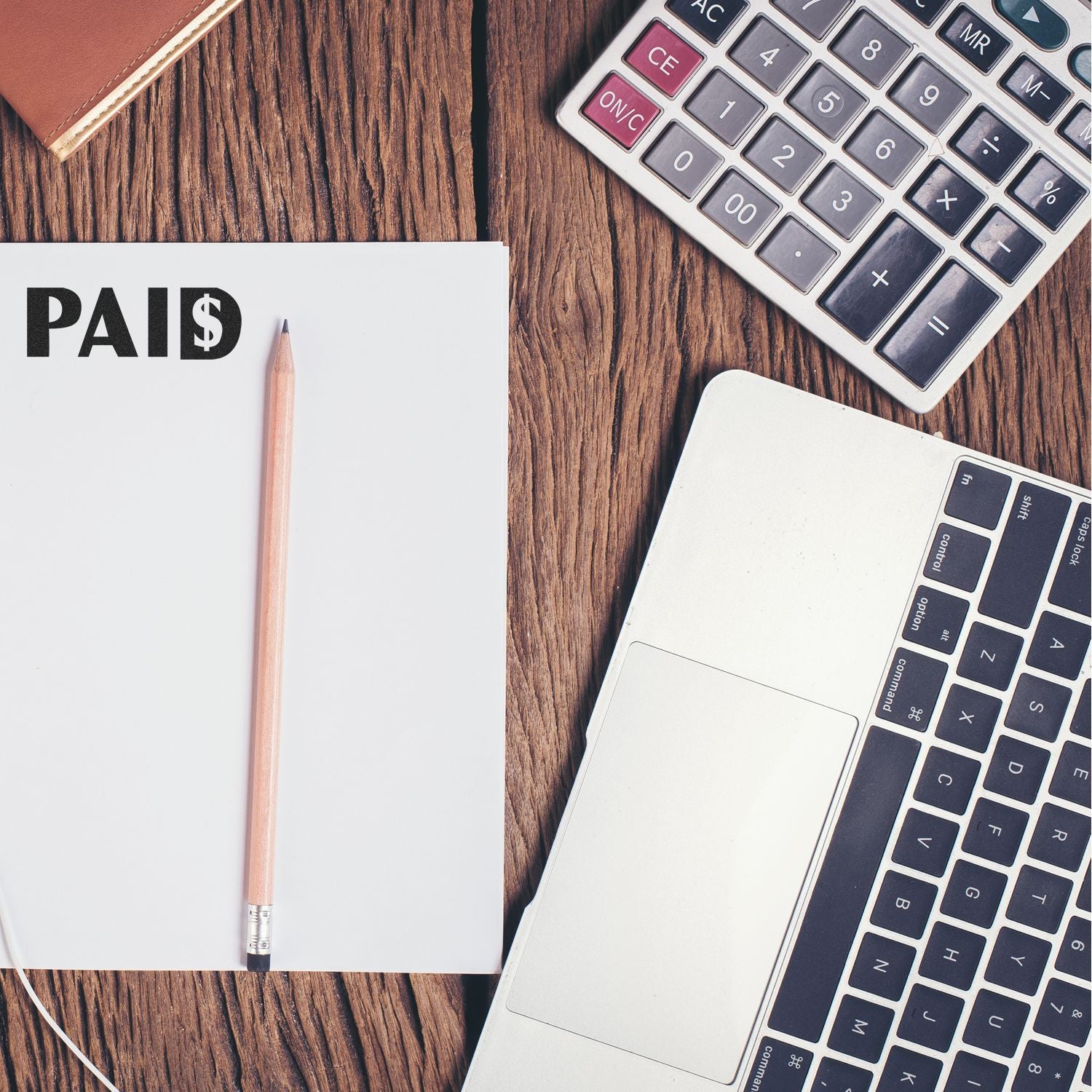 Paid invoice concept with calculator, laptop keyboard, and PAID note on wooden desk for accounting and billing