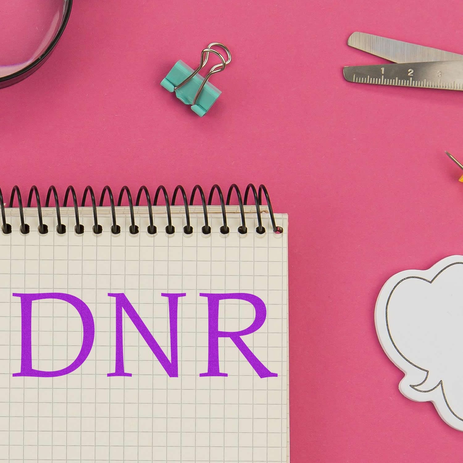 DNR text on a spiral notebook with office supplies on a pink background