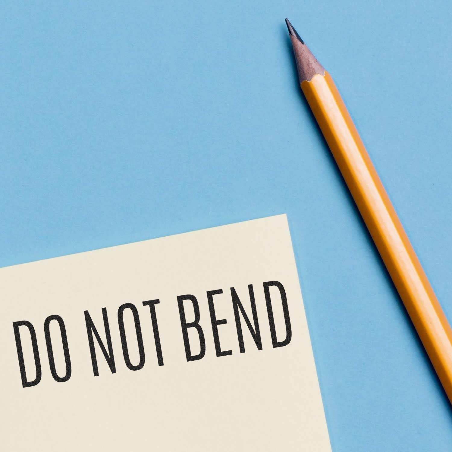 Close-up of pencil and DO NOT BEND label on a blue background, office shipping and packaging concept.