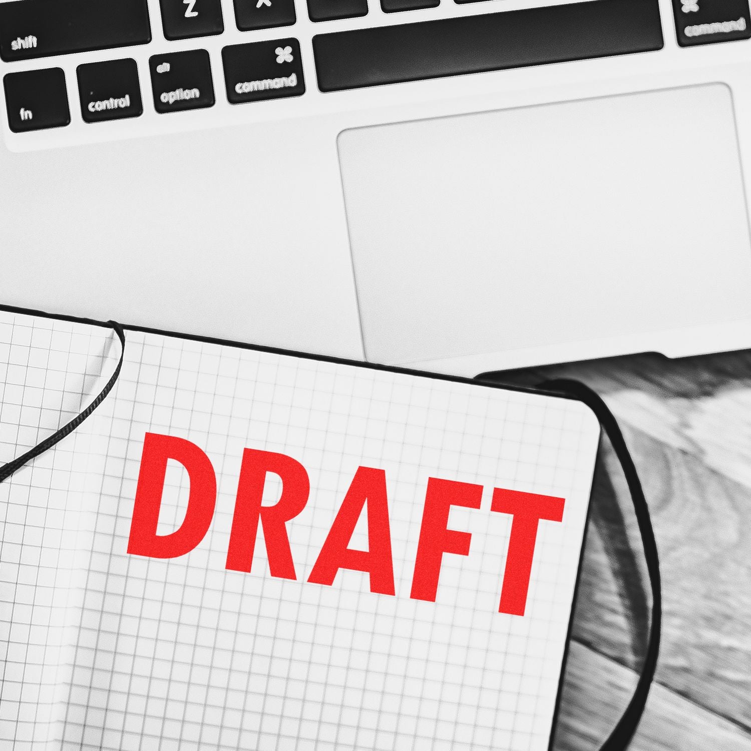 Red DRAFT notebook beside a laptop keyboard, representing document editing and writing work.