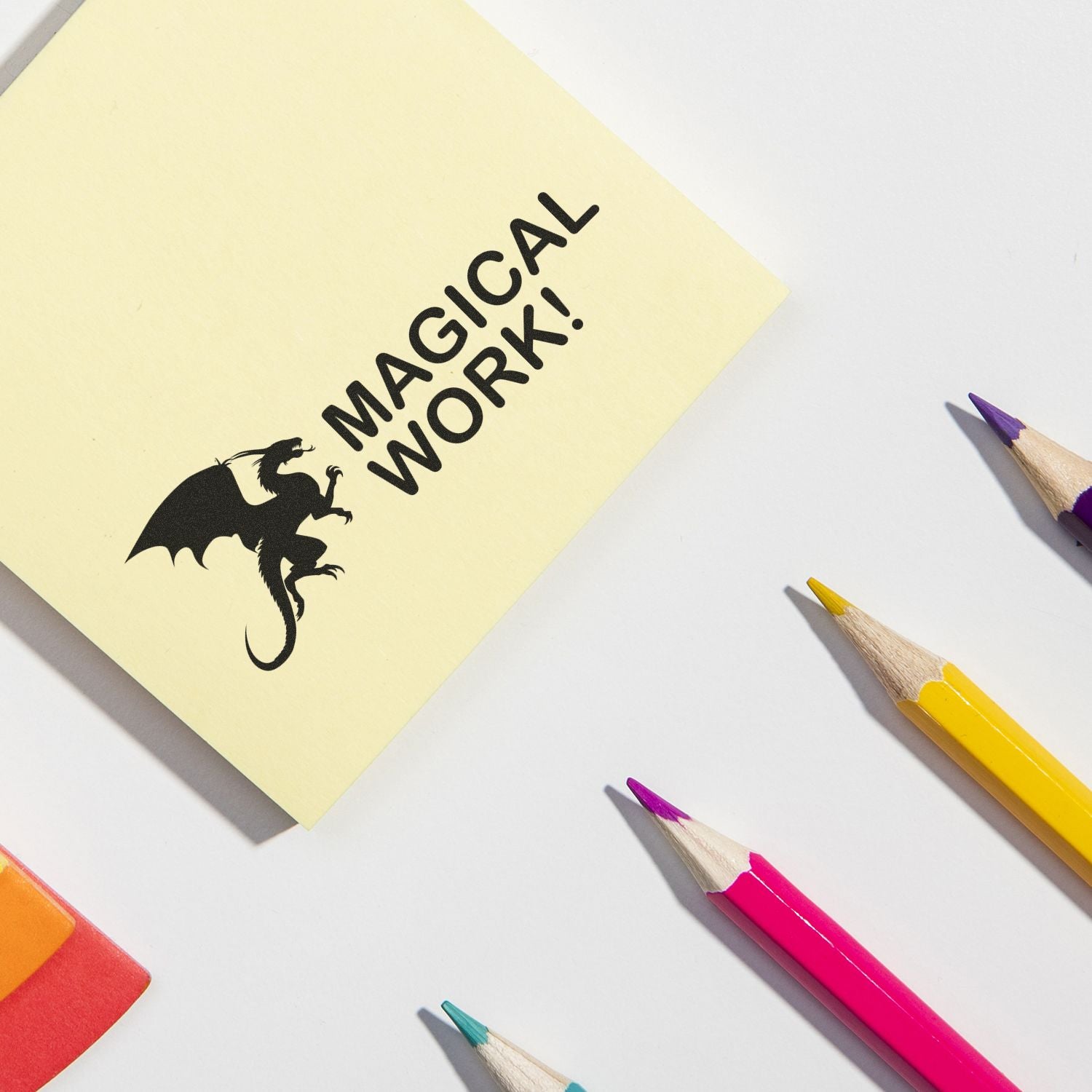 Magical work stationery design on yellow sticky note with dragon silhouette and MAGICAL WORK! text, surrounded by colored pencils.