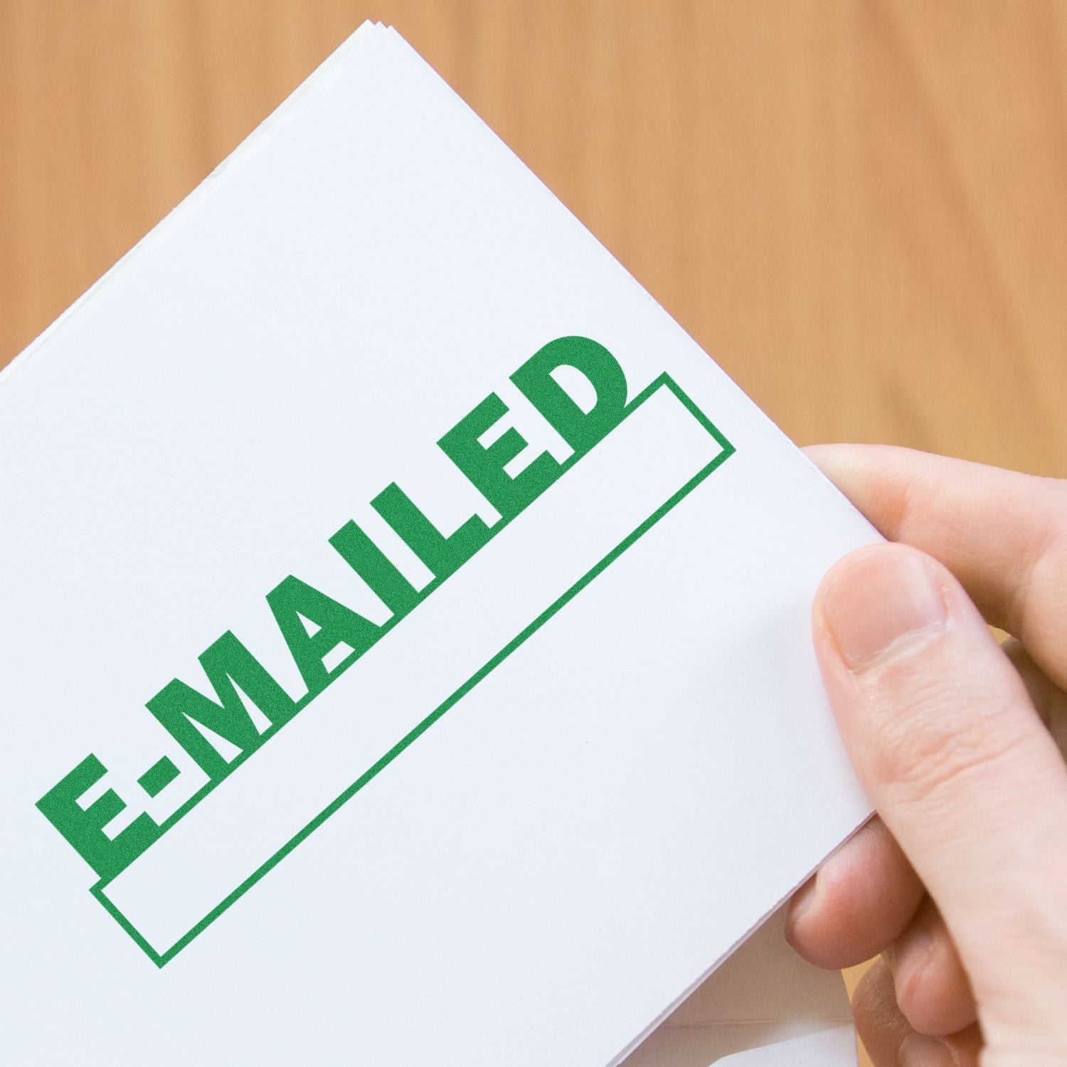 Hand holding a white envelope stamped E-MAILED in green, showing digital document delivery confirmation.