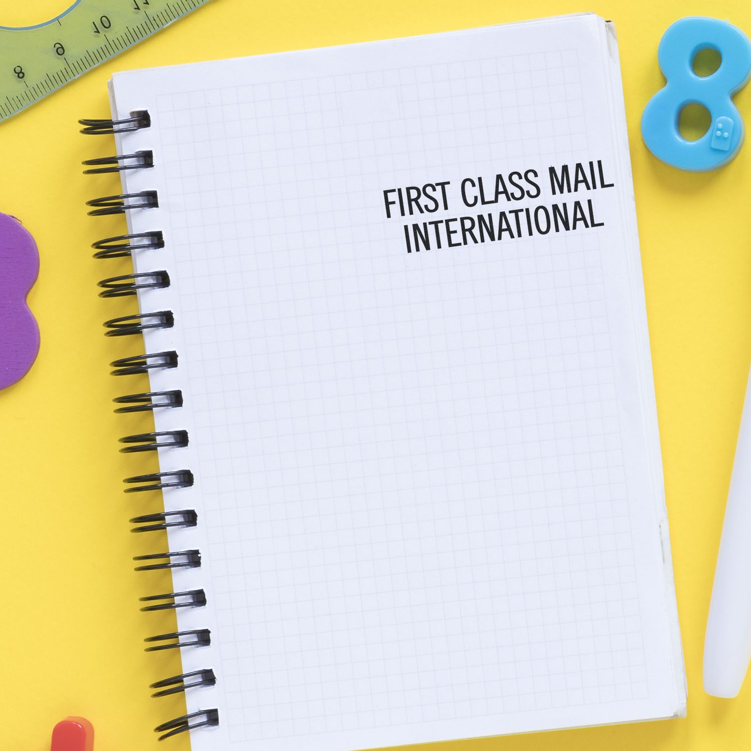 Notebook with First Class Mail International text on a bright yellow background with colorful school stationery items.