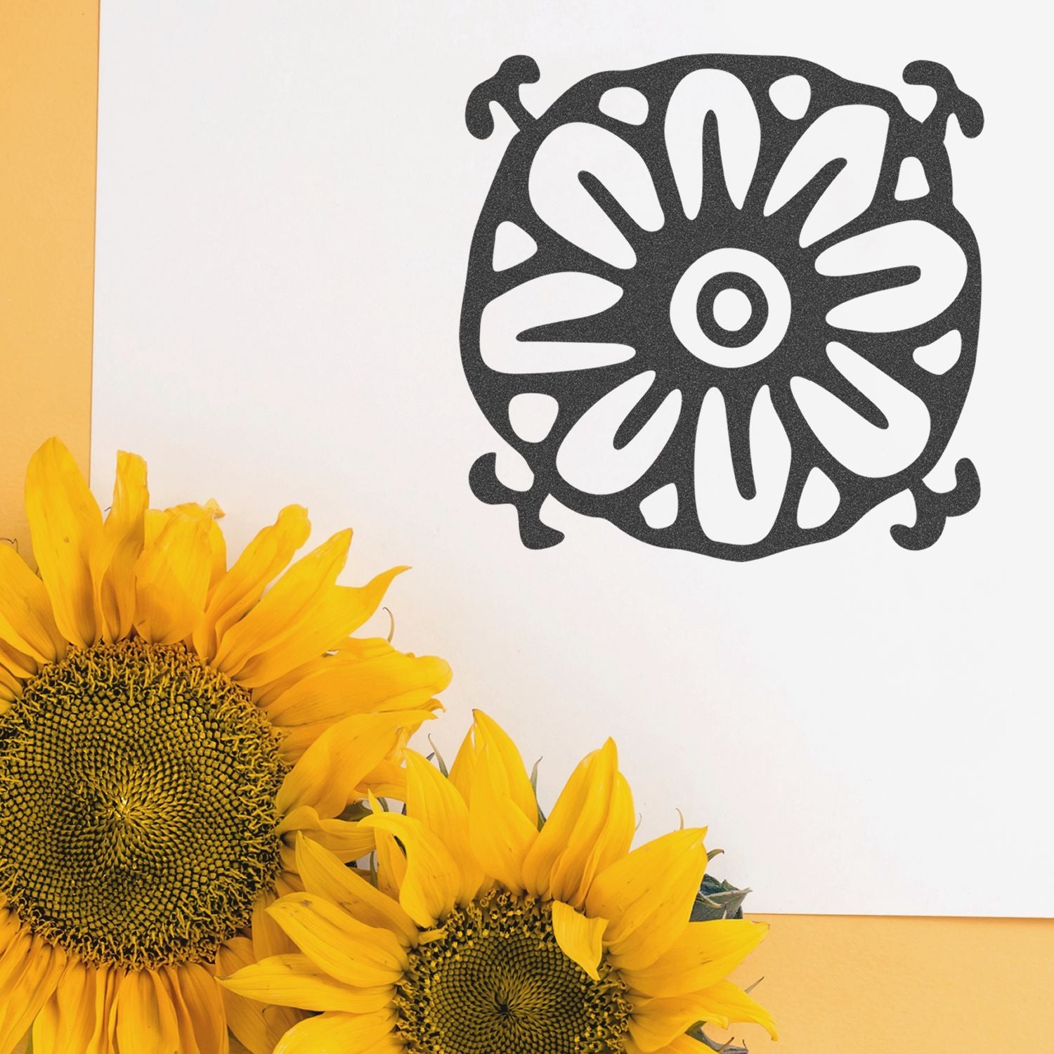 Sunflower blooms with black floral mandala design on a white card against a yellow background.