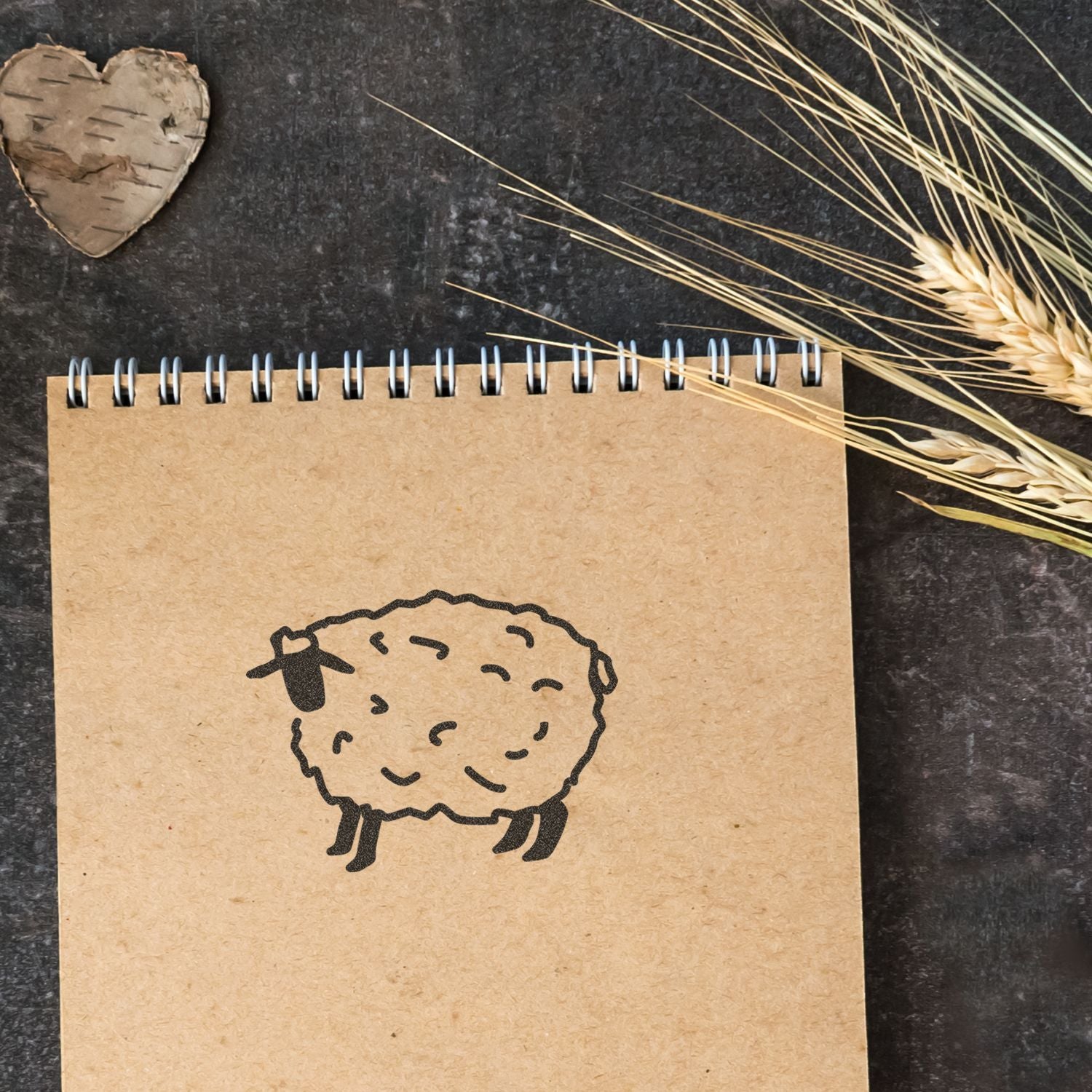 Rustic kraft notebook with sheep doodle, wheat stalks, and birch heart on a dark background.