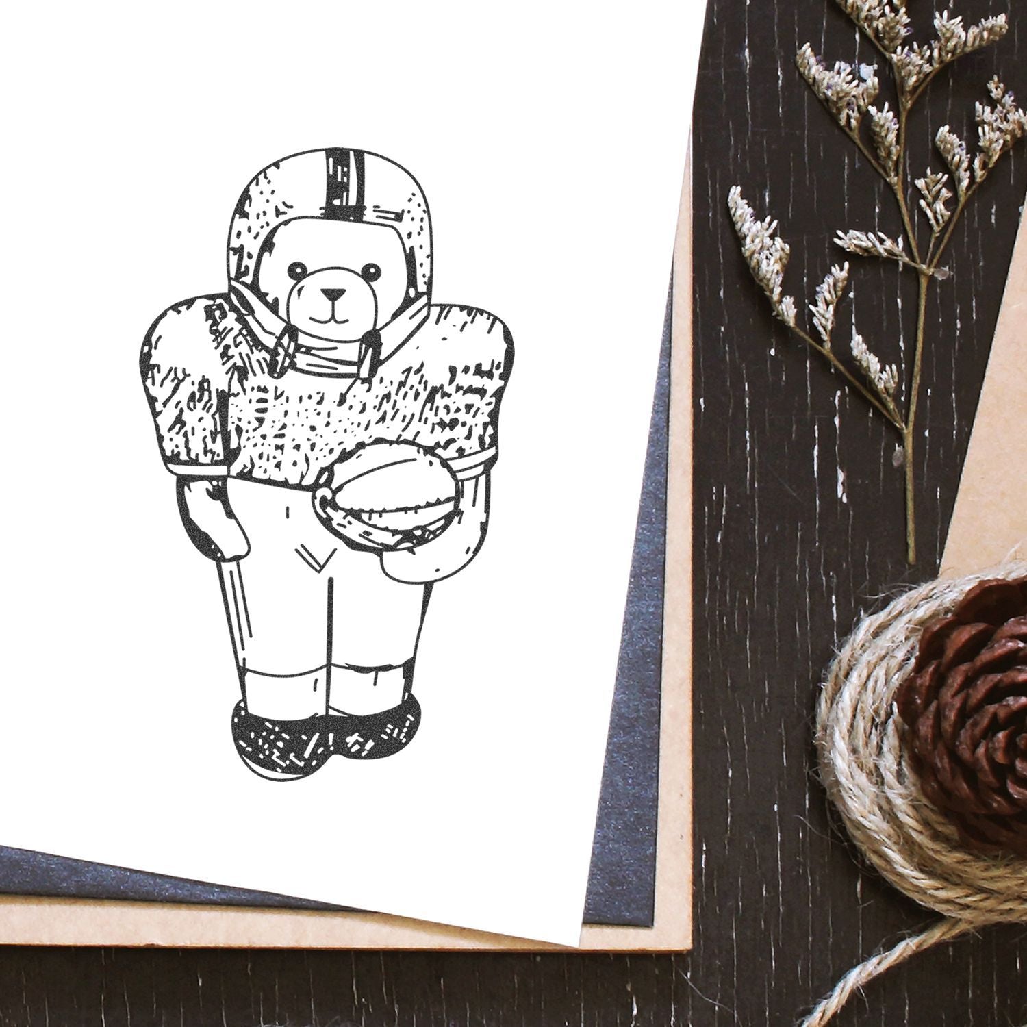 Cute teddy bear football player illustration on white paper with rustic pinecone and dried floral decor on a dark wood background.