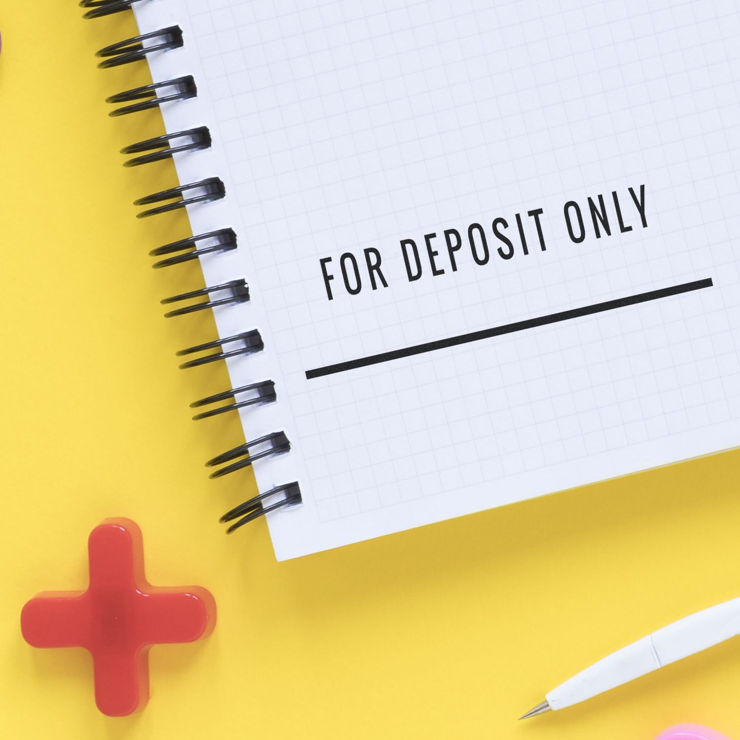 Bank deposit slip with For Deposit Only stamp, pens and notepad on yellow background indicating deposit instructions only.