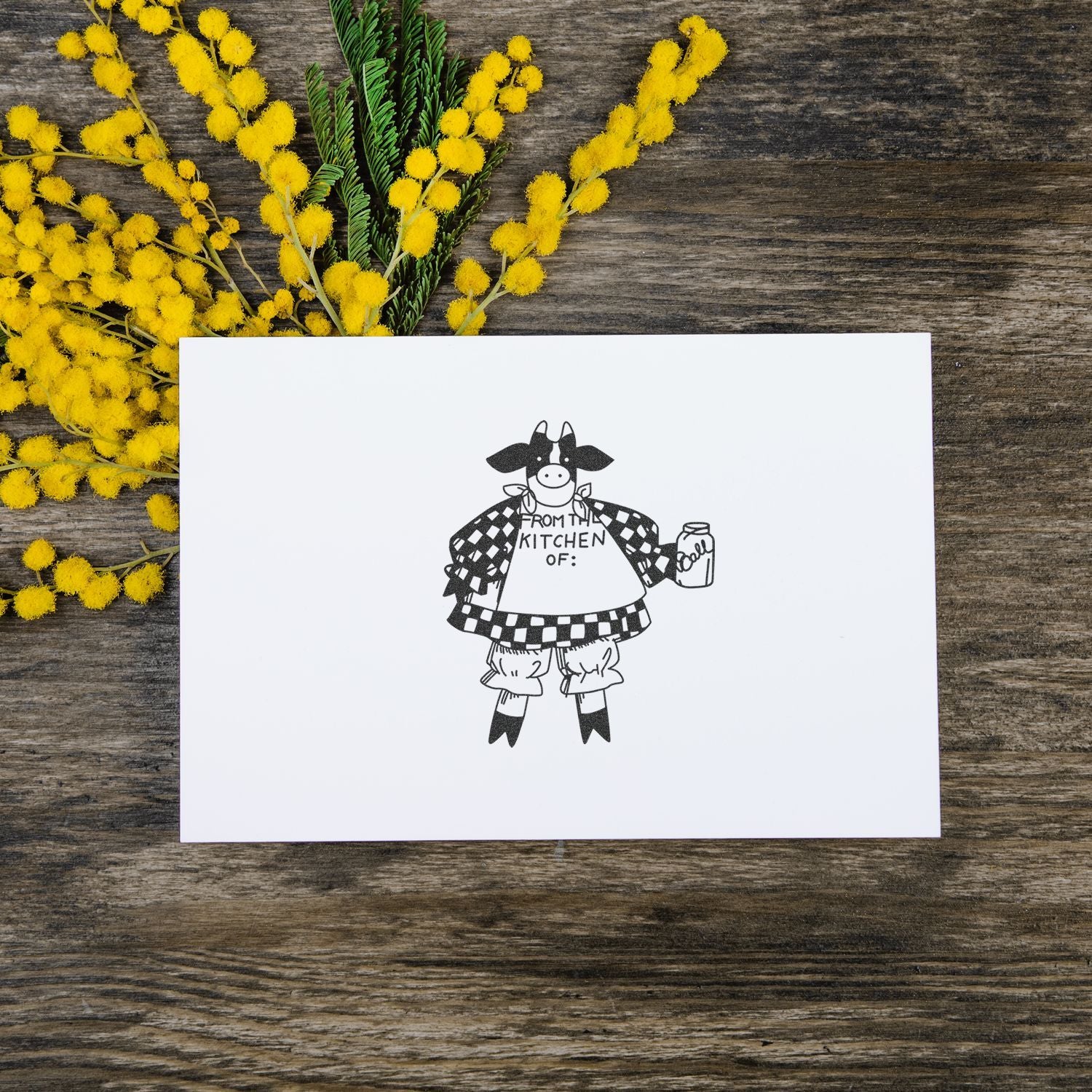 Blank greeting card with cow illustration and yellow mimosa flowers on rustic wooden table