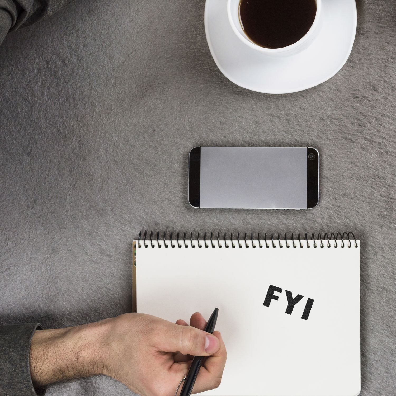 Man writing FYI on a notebook at a desk with coffee and smartphone, representing business note-taking and productivity.
