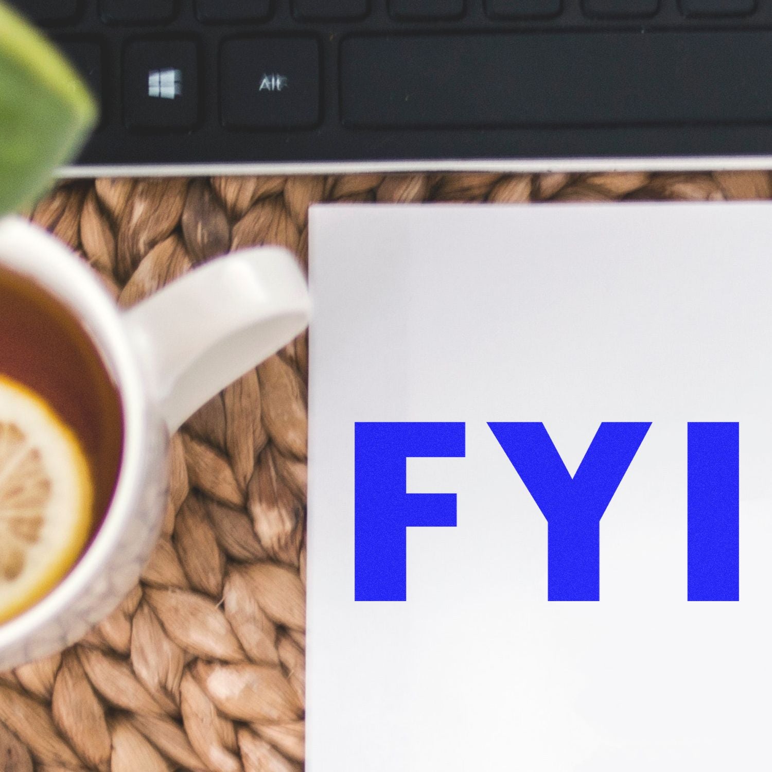 FYI notice paper on a desk beside laptop keyboard and coffee cup, highlighting business updates and office communication today.