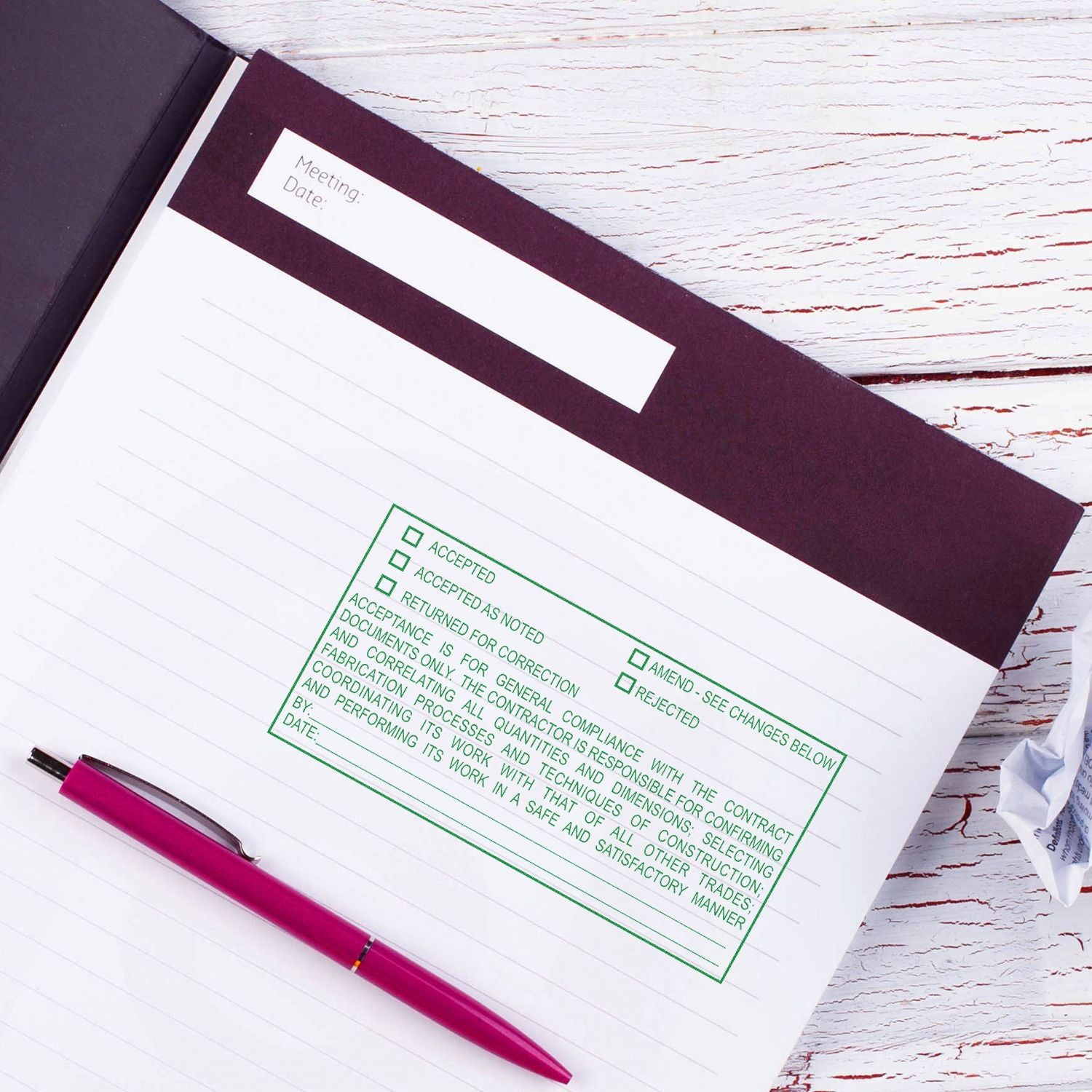 Open meeting notebook with pink pen and approval stamp on white wooden desk.