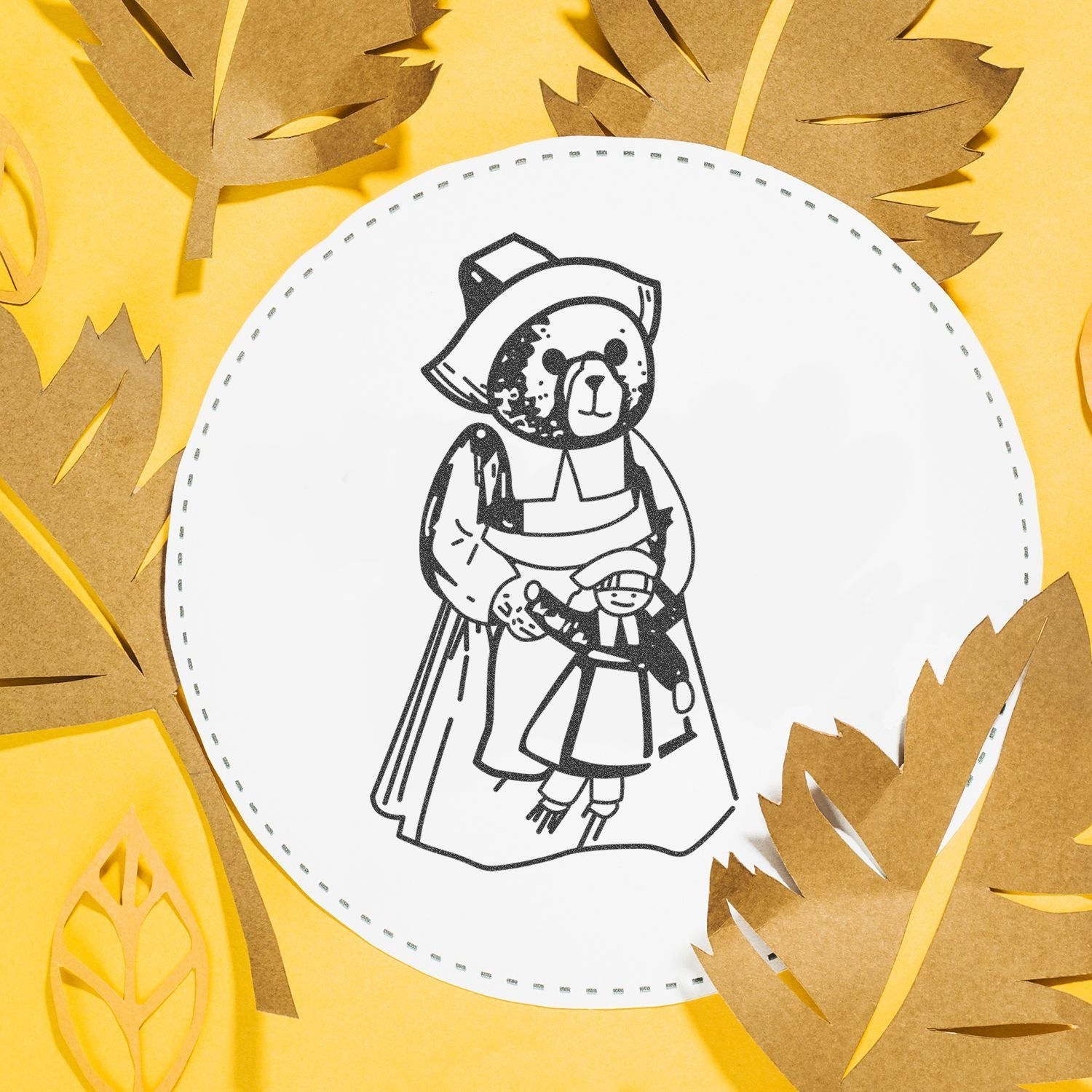 Handmade teddy bear illustration on a white embroidery hoop surrounded by gold autumn leaves on a yellow background.