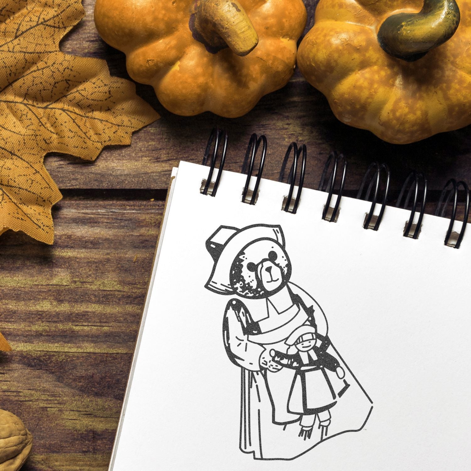 Autumn-themed spiral notebook with cute bear illustration, decorative pumpkins, and fall leaves on a rustic wooden table.