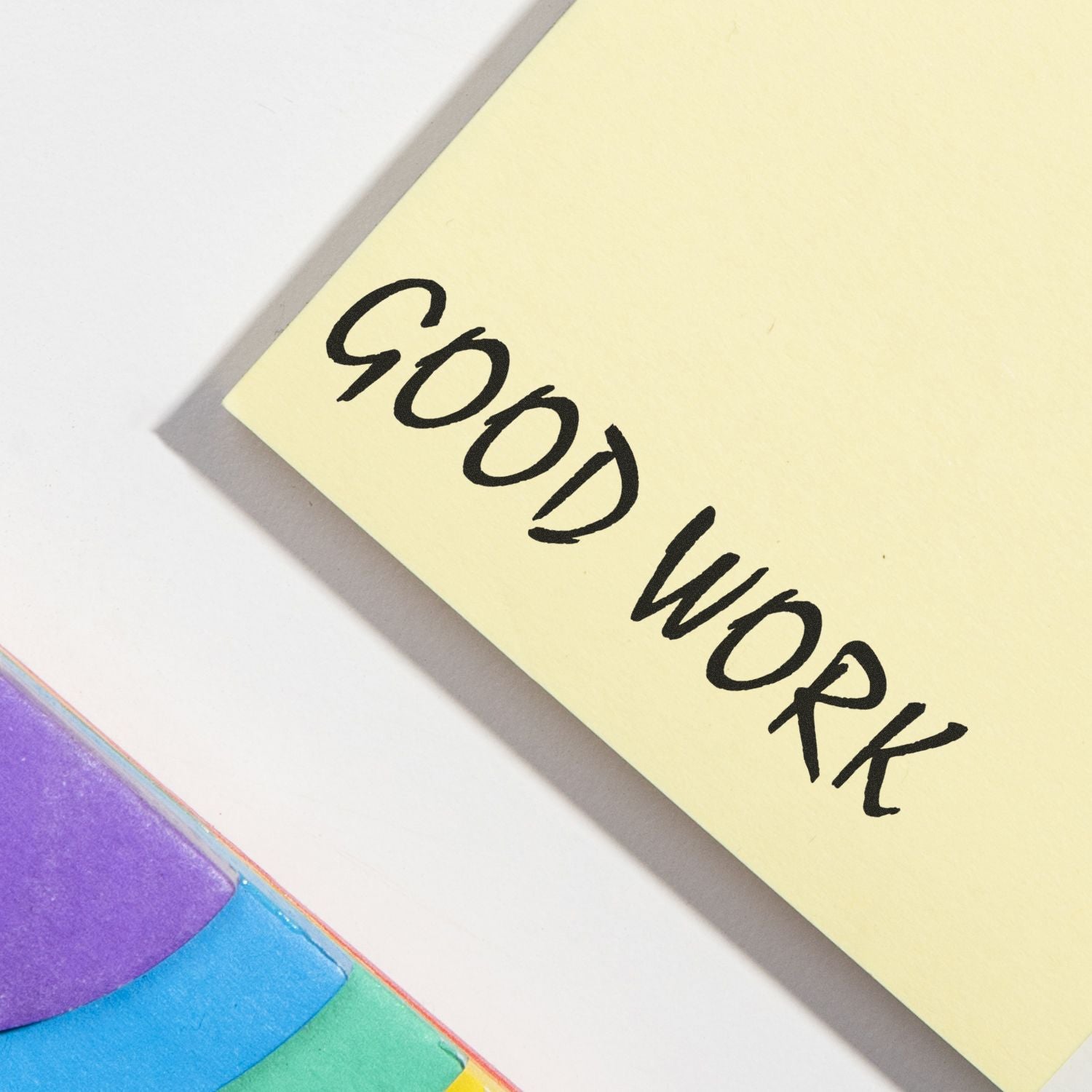 Yellow sticky note with good work handwritten in black marker on a colorful paper background.