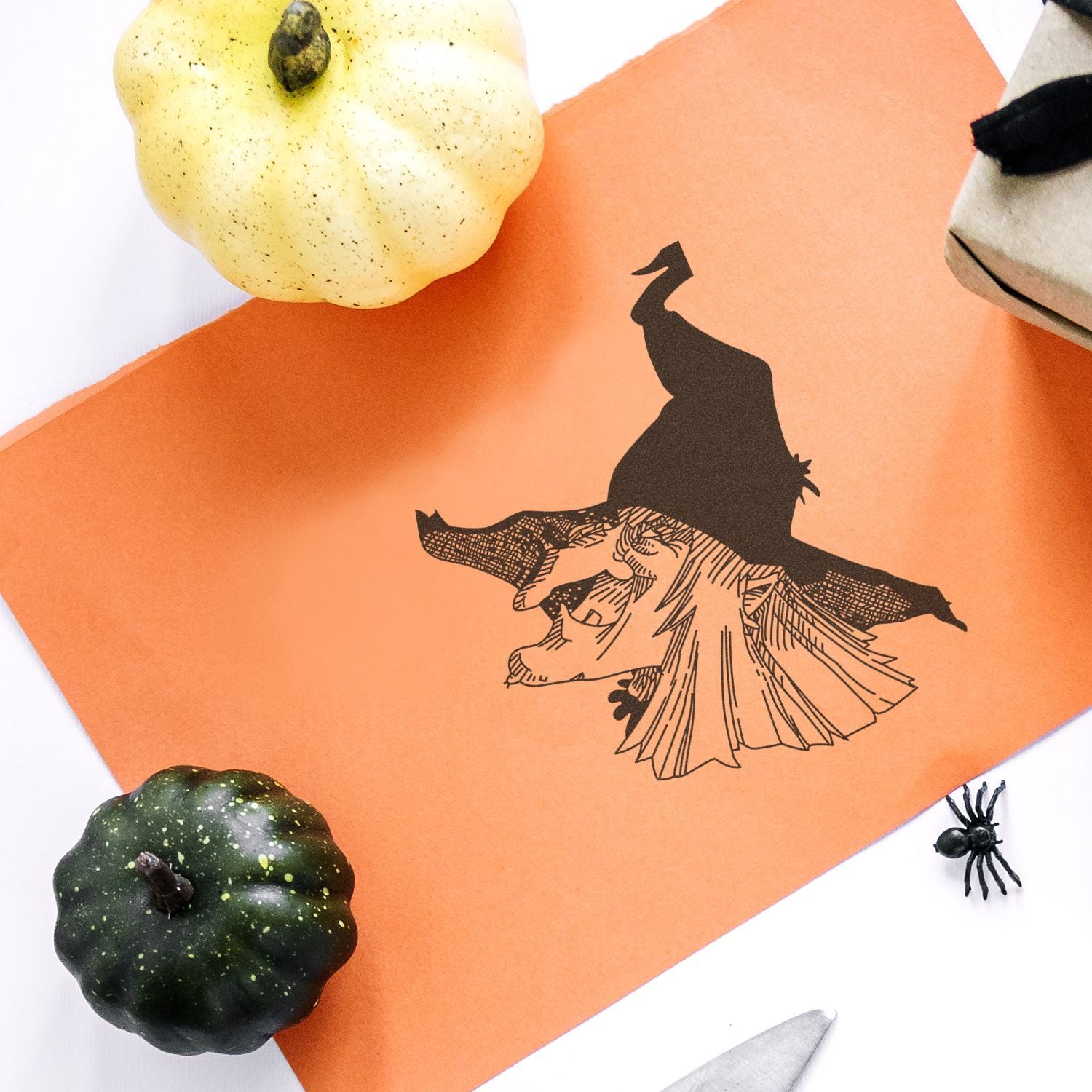 Halloween craft with witch silhouette on orange paper, surrounded by decorative pumpkins and a spider on a white background