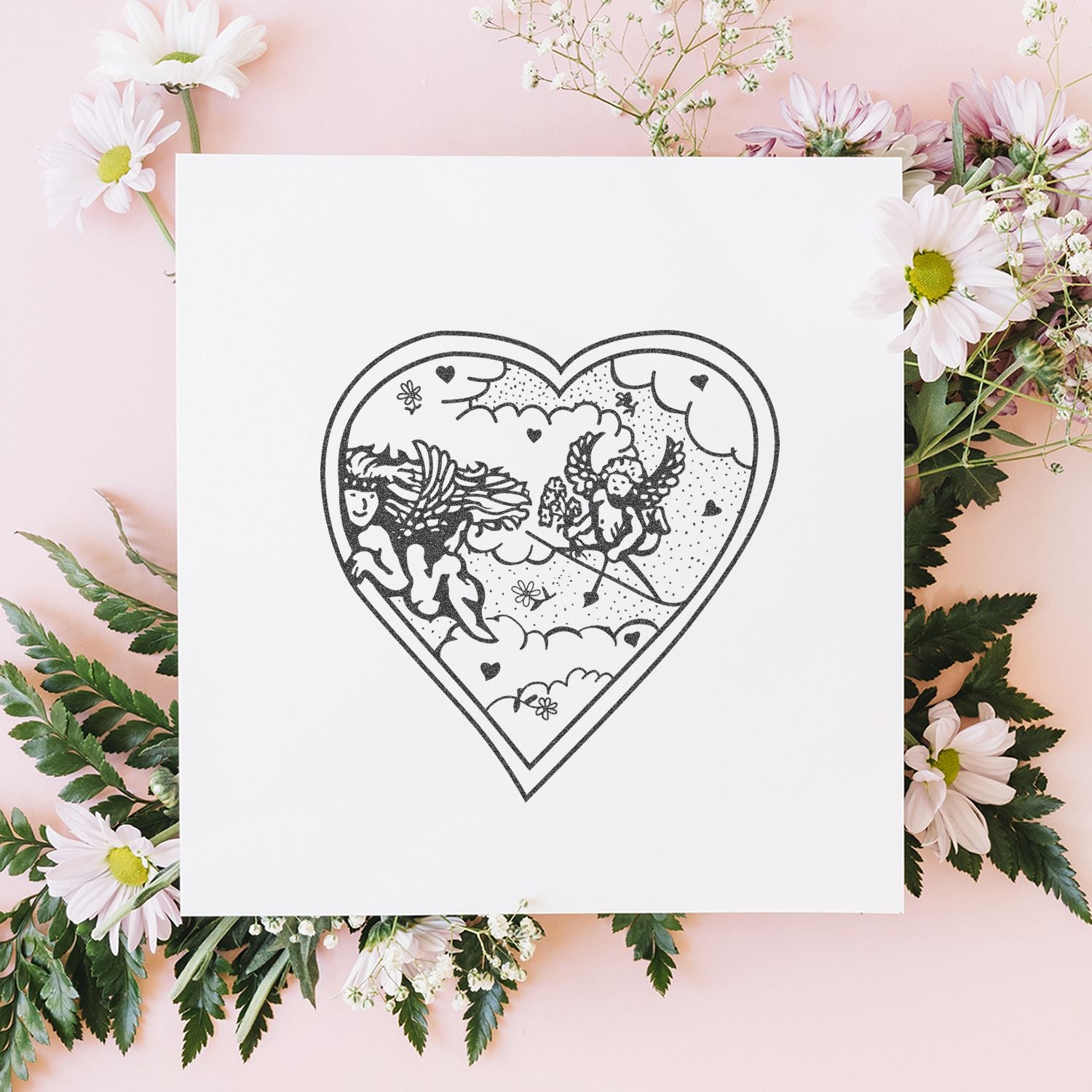 Heart-shaped black line art with angels on a white card, surrounded by pink daisies and greenery on a pastel pink background.