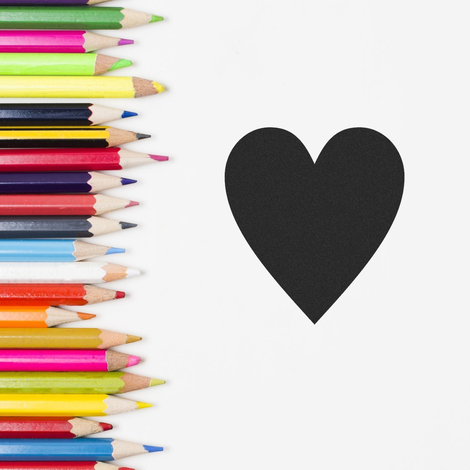 Colorful colored pencils arranged beside a black heart on a white background, creative art concept.