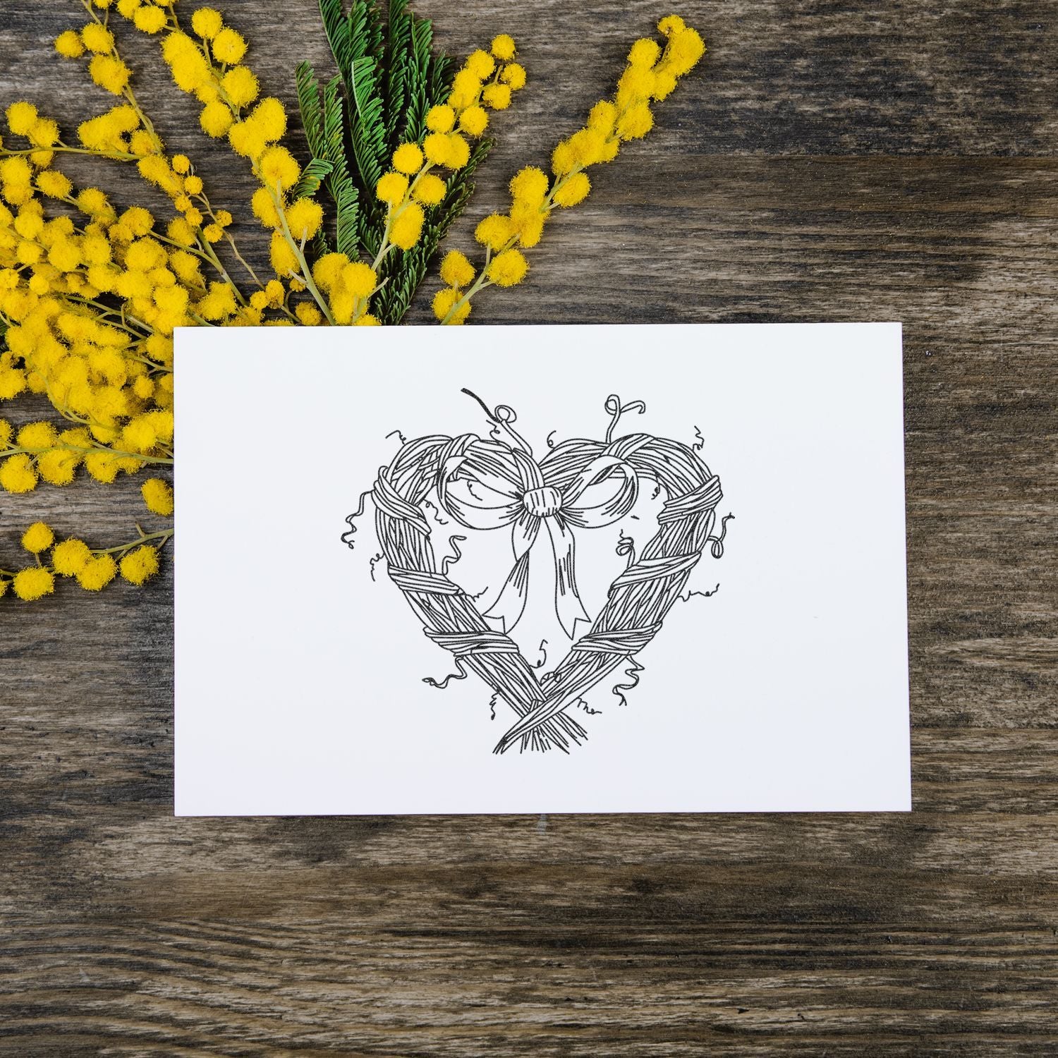 Handmade floral heart wreath greeting card with yellow mimosa flowers on rustic wooden background