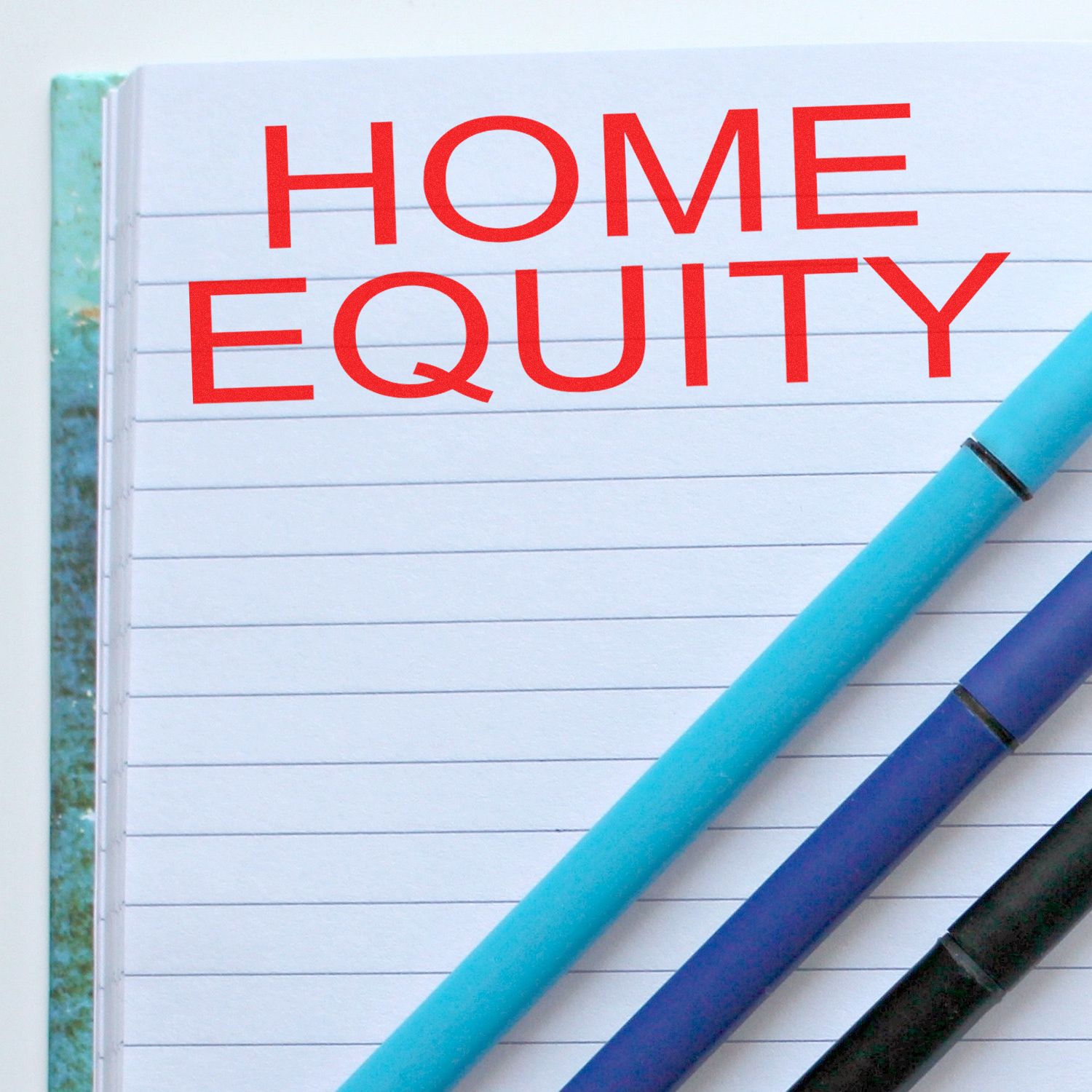 Notebook page reading HOME EQUITY with pens, illustrating real estate home equity financing and savings.