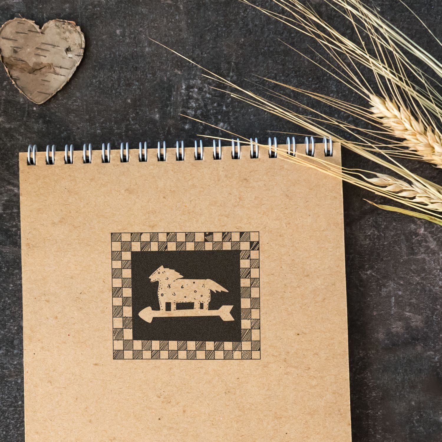 Rustic kraft spiral notebook with wooden heart, dried wheat, and minimalist farm animal design on a dark background.