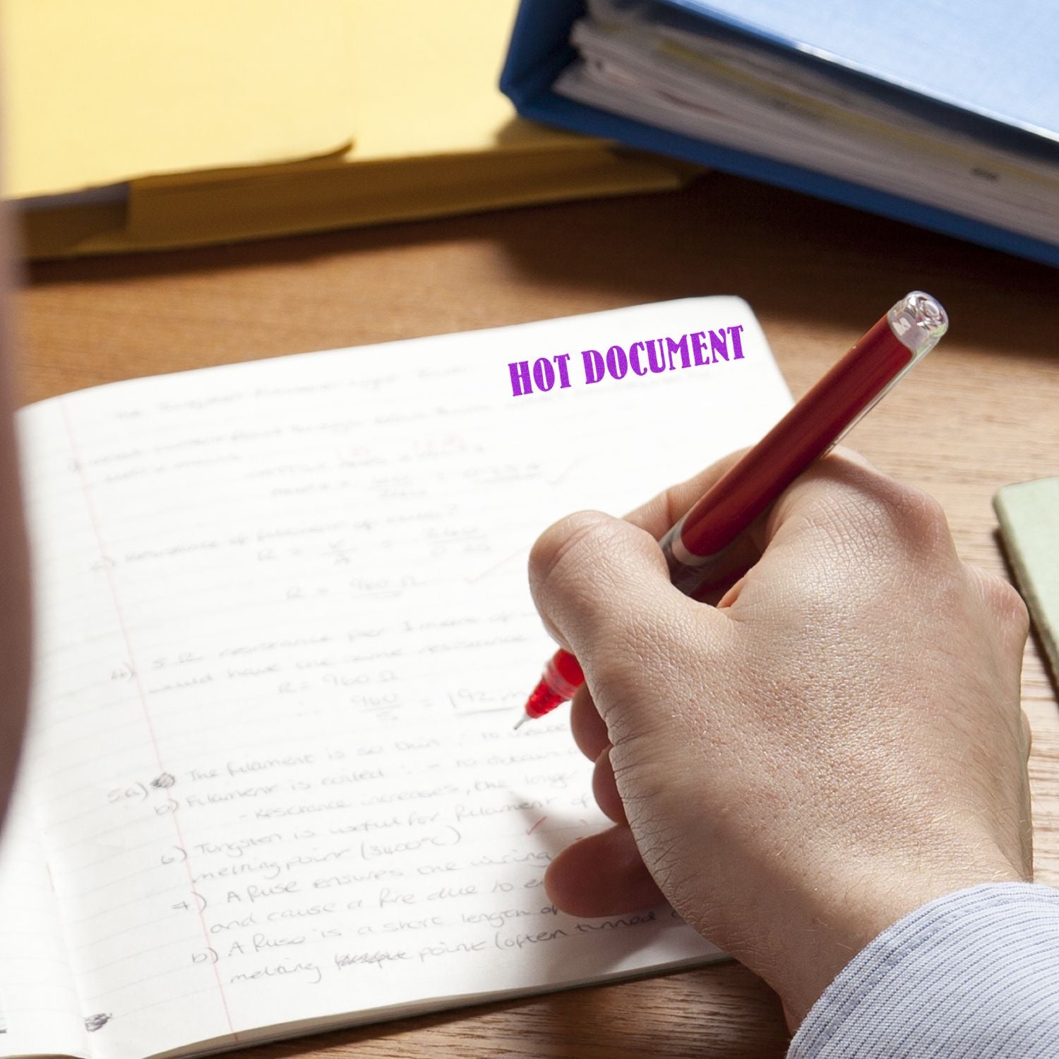 Hand writing on hot document paper with a pen; HOT DOCUMENT label over notebook and files on office desk.