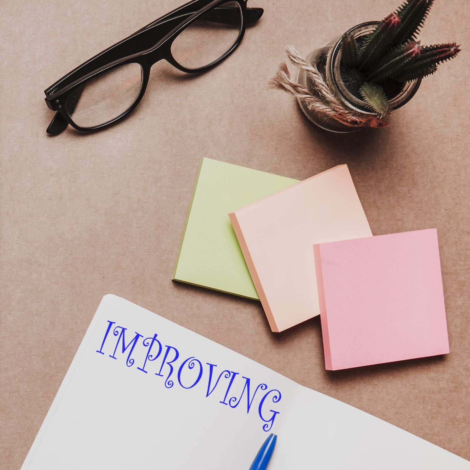 Creative workspace flat lay with eyeglasses, sticky notes, notebook, pen, and potted succulent on a brown desk.