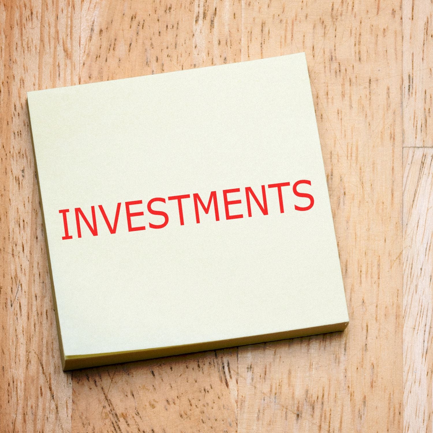 INVESTMENTS text on white card on wood background, illustrating investment planning and finance concepts.