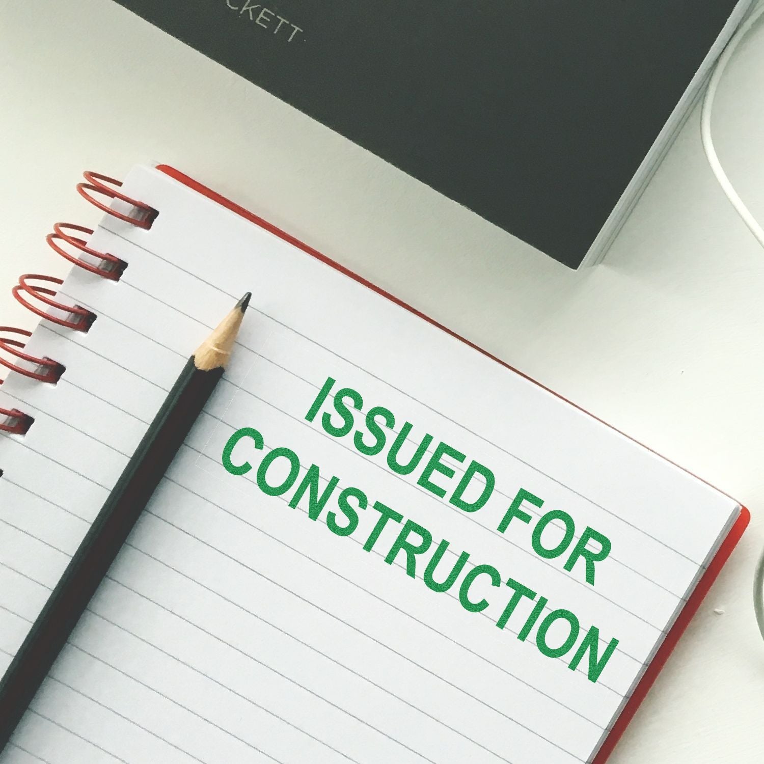 Notebook with pencil and Issued for Construction text, representing construction planning and project documentation.
