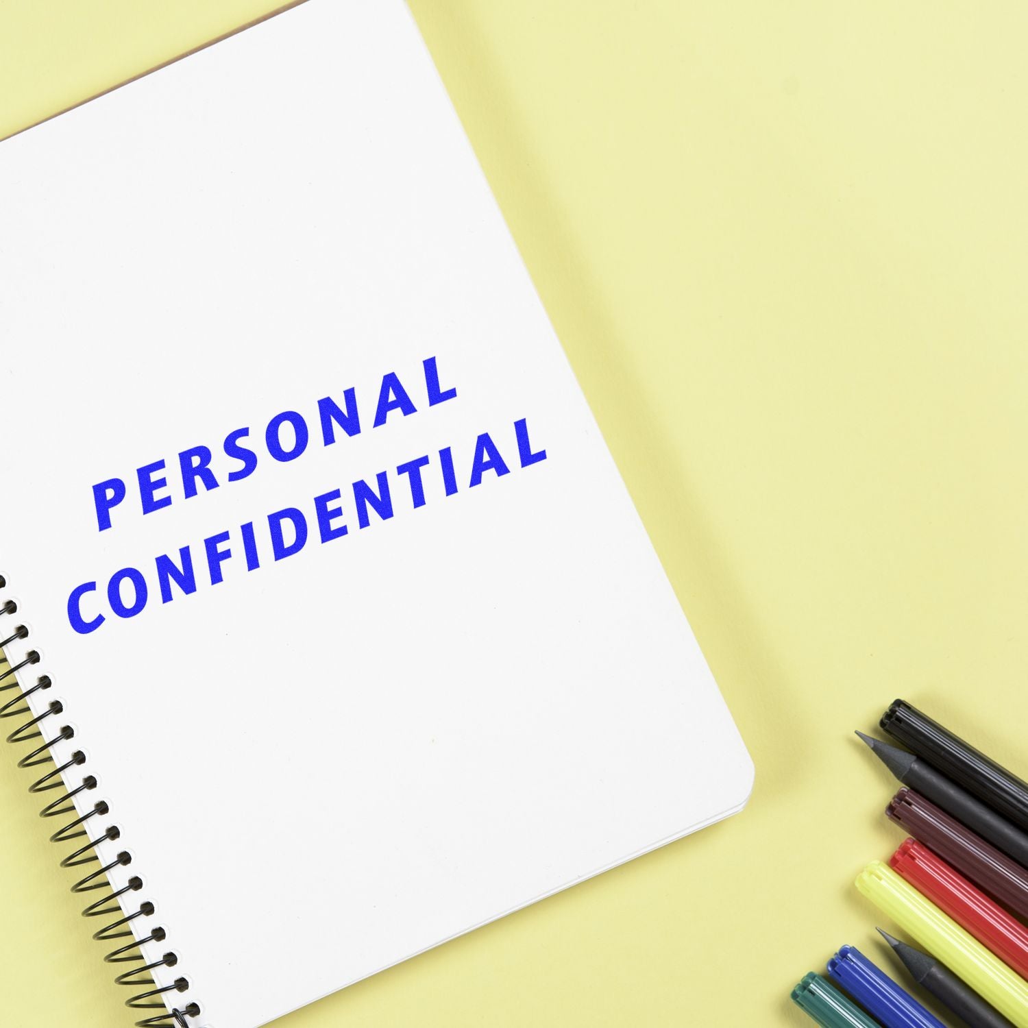 Personal confidential notebook with colorful pens on yellow background, business privacy concept.