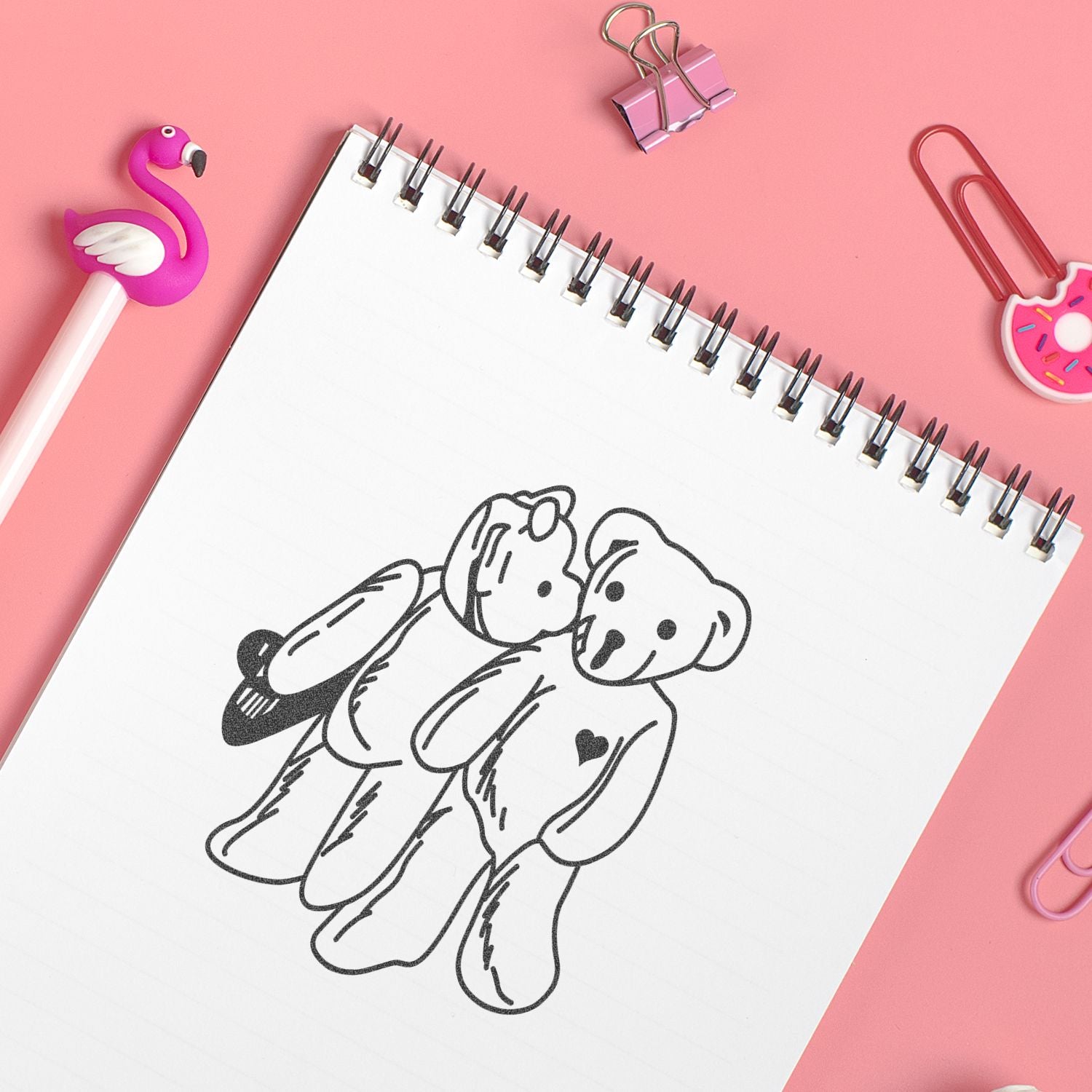 Cute teddy bear doodle in spiral notebook with pink stationery and flamingo pen on pastel pink background.