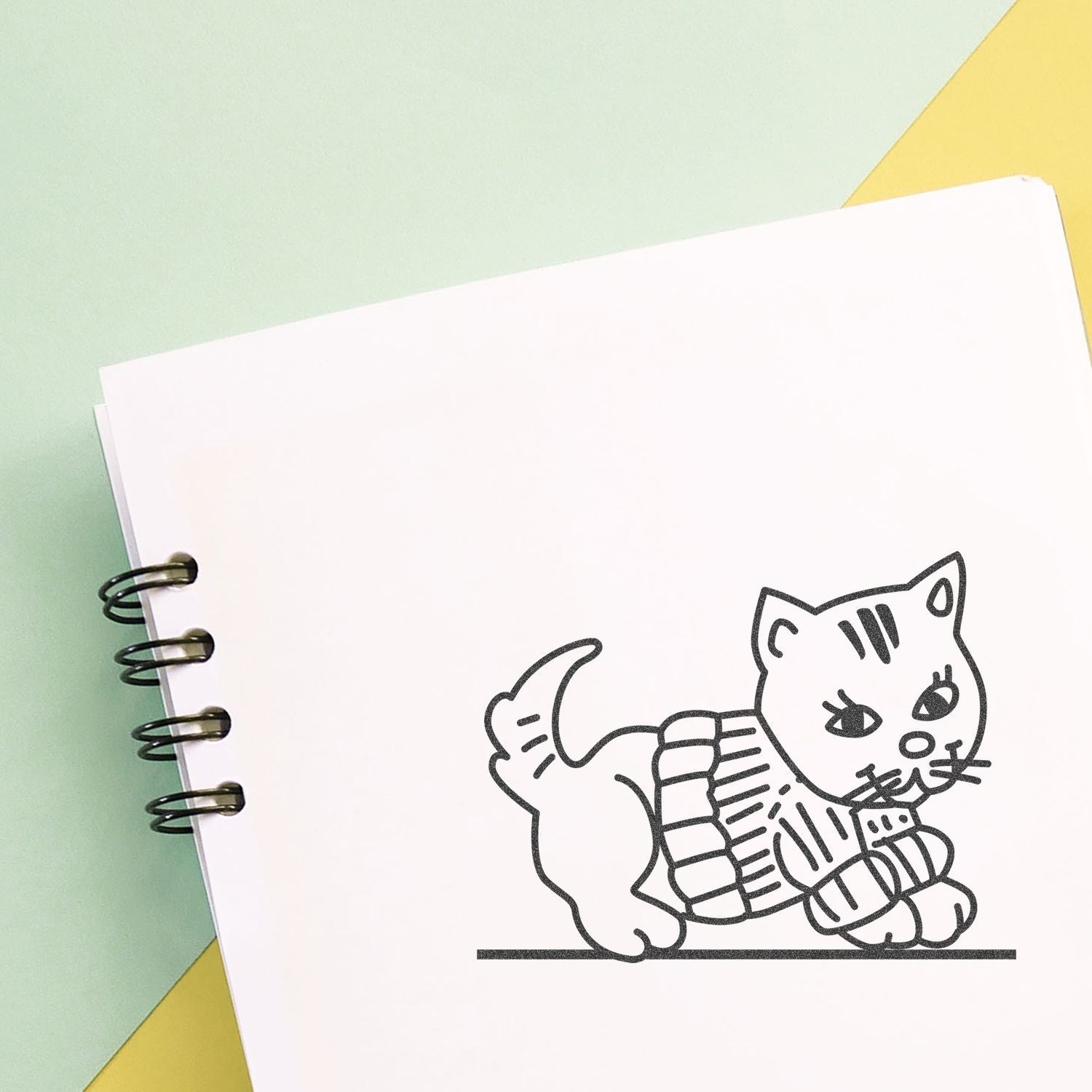 Cute cat sketch on a blank spiral notebook with pastel green and yellow background.