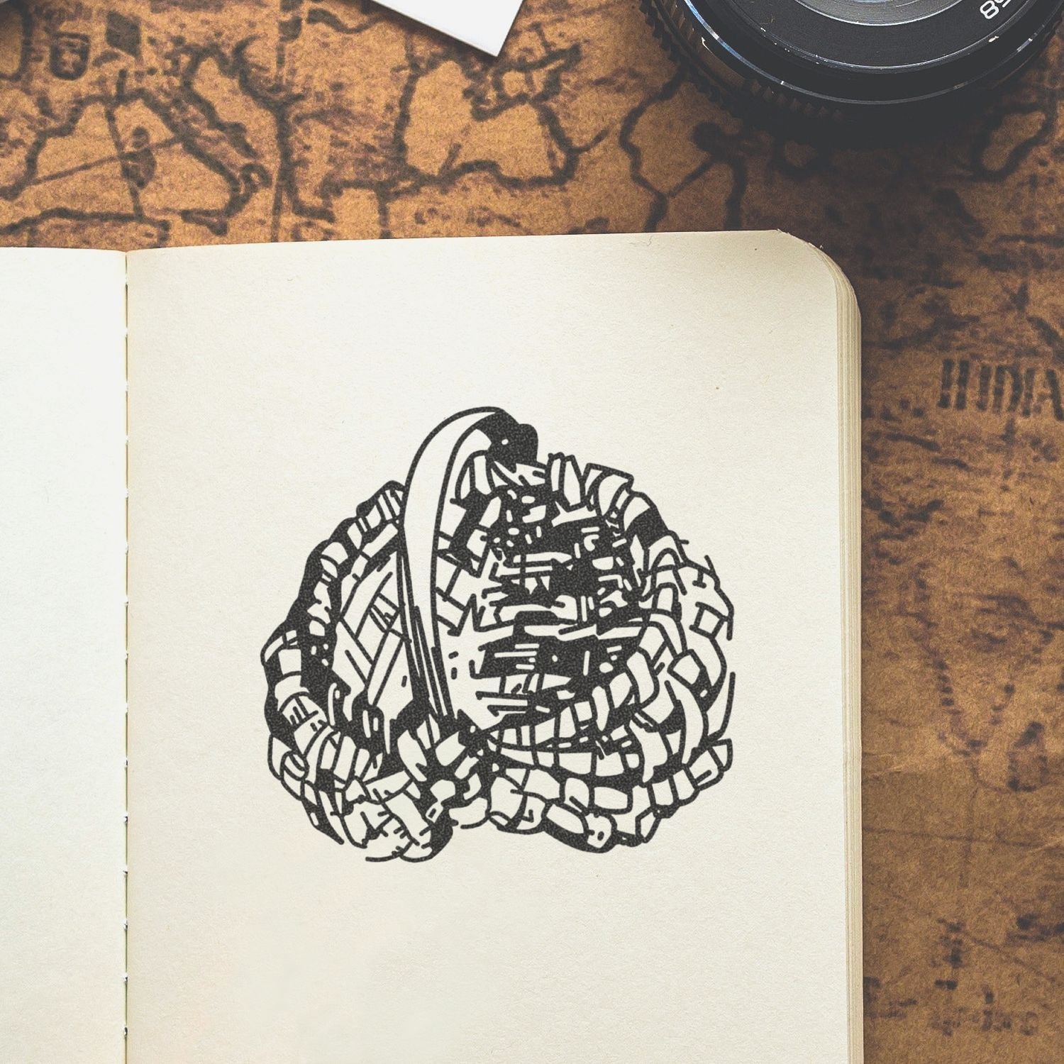 Open sketchbook with abstract black ink illustration on cream paper, styled on a vintage map background with a camera lens.