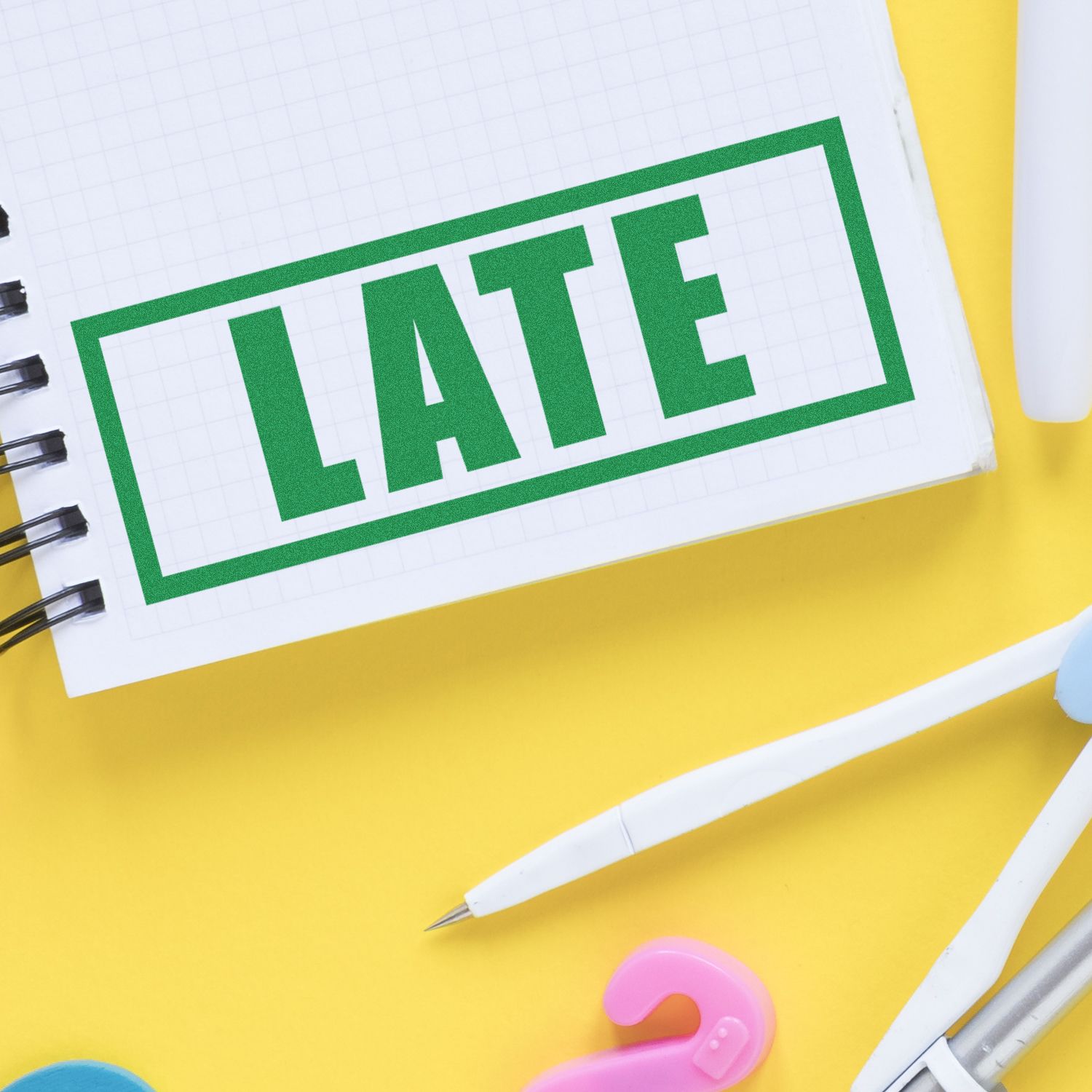 Close-up of green LITE text on a notebook page with grid paper, pencils, and desk supplies on a yellow background.