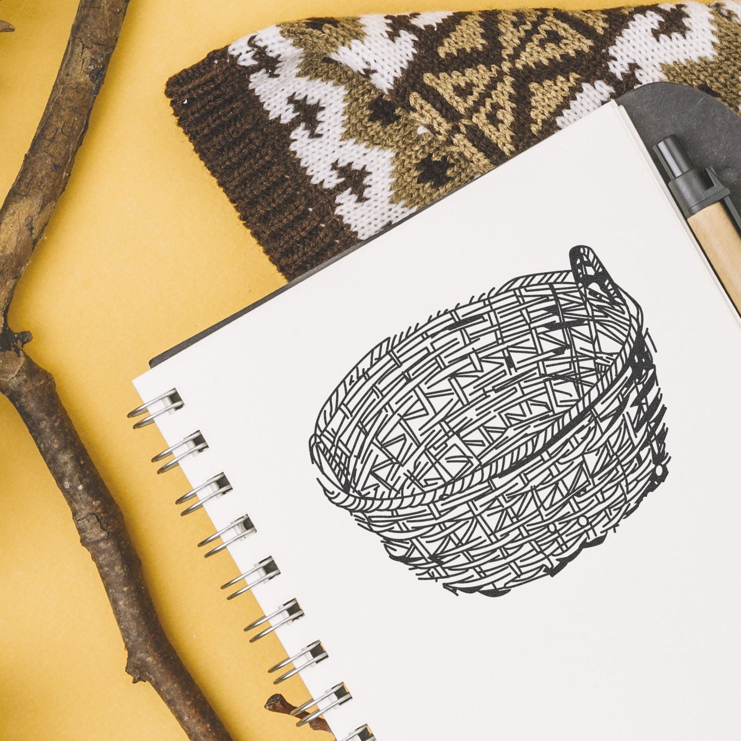 Sketchbook with a hand-drawn woven basket illustration, knitted pattern fabric, and rustic branches on a yellow background.