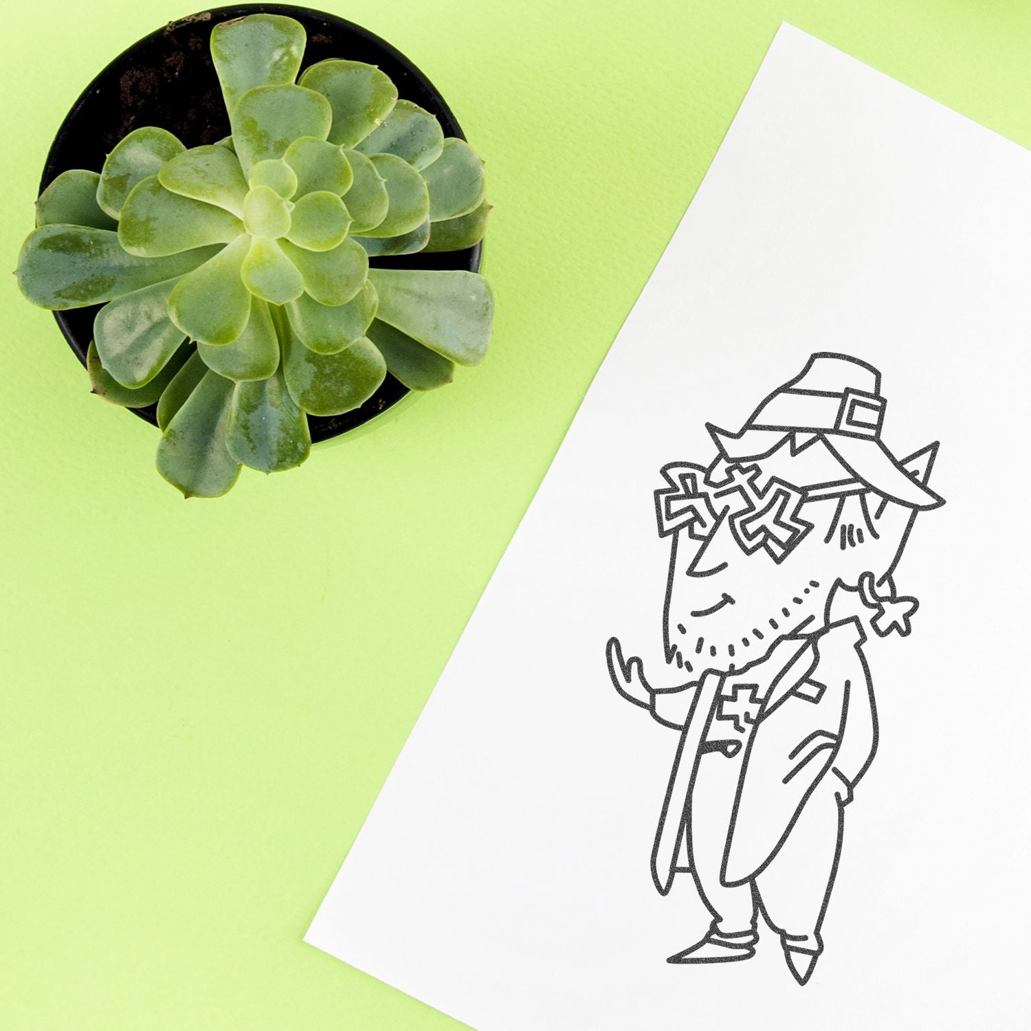 Top view of a green succulent in a black pot next to a Halloween witch line art drawing on a light green background.