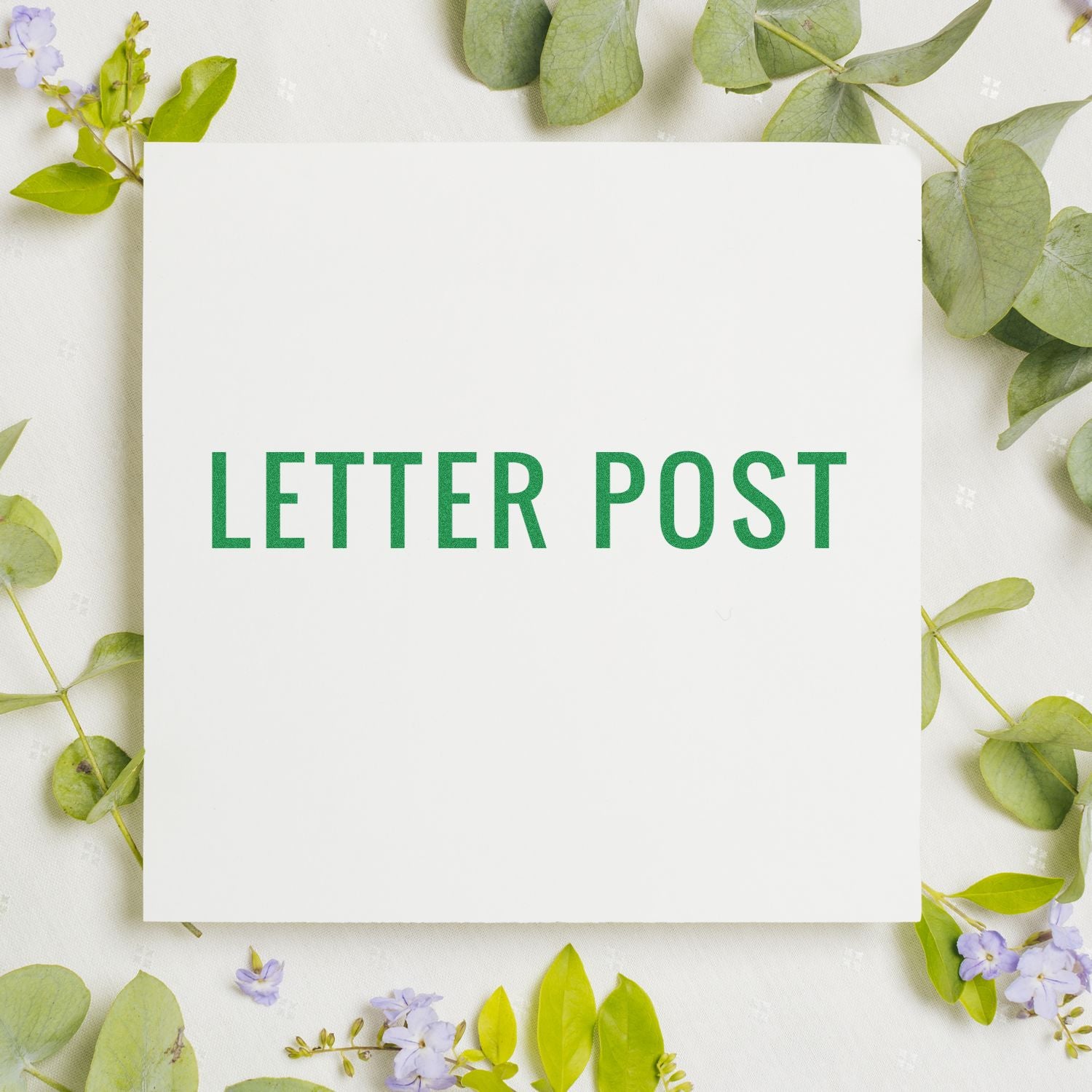 Blank letter post card surrounded by eucalyptus leaves and delicate flowers on a light floral flat lay background