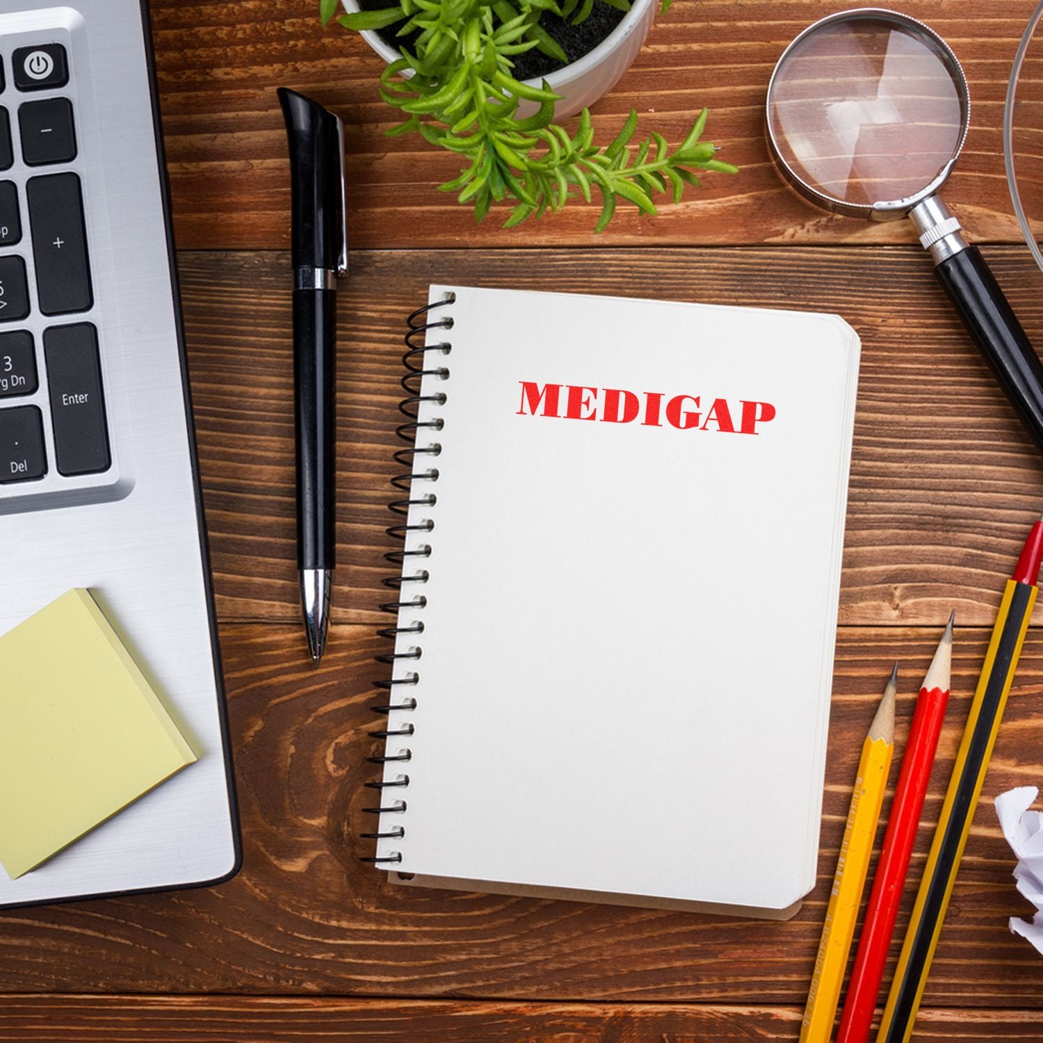 Medigap insurance research concept: notebook marked MEDIGAP with magnifying glass, pens, and computer on desk.