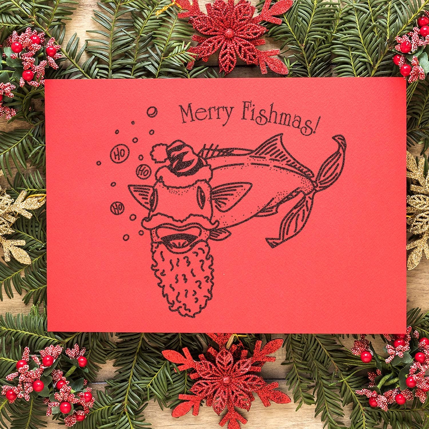 Red Merry Fishmas holiday card with festive fish Santa illustration surrounded by Christmas greenery and decorations