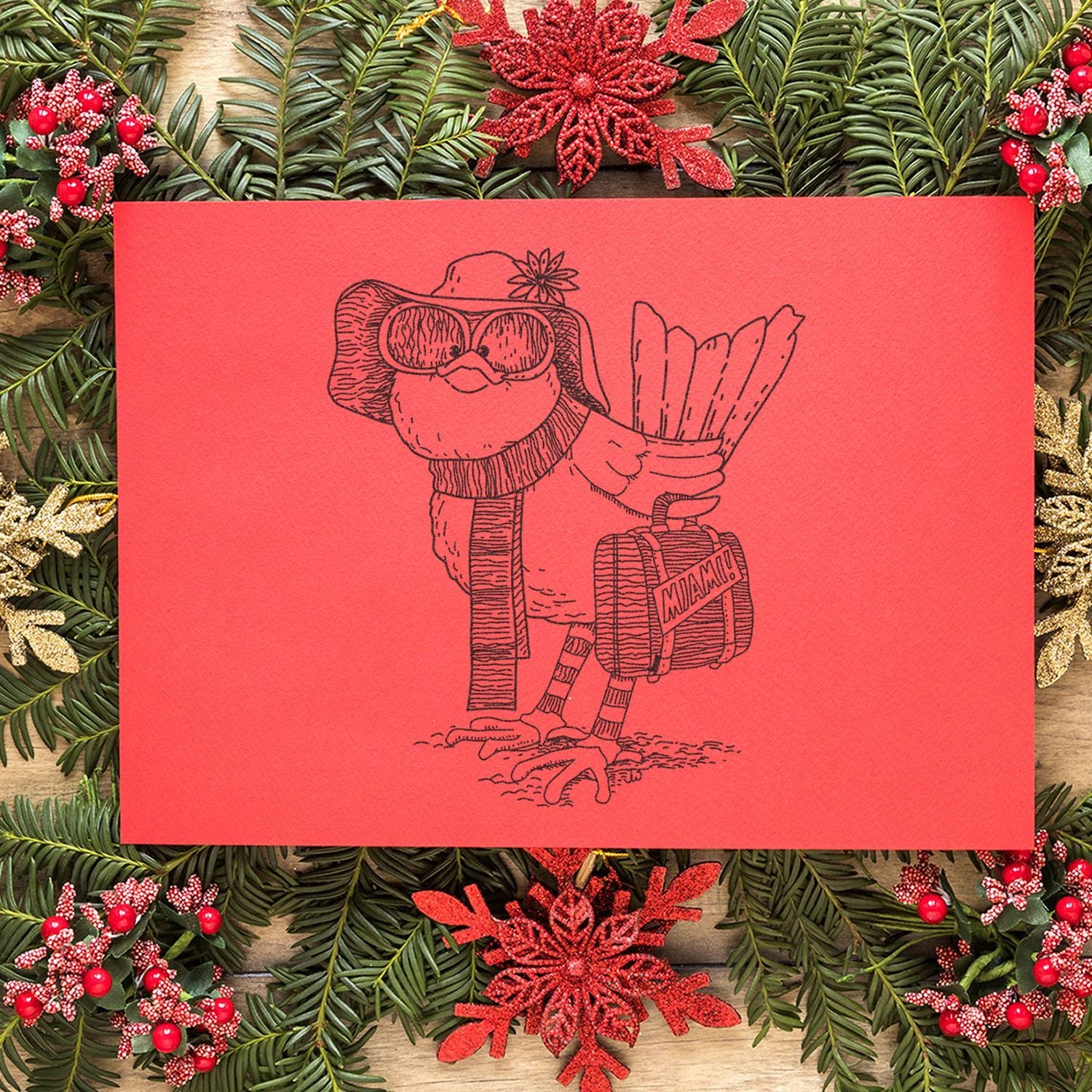 Festive Christmas card with a whimsical bird wearing a hat and sunglasses, holding a Miami suitcase, surrounded by holiday greenery and red decorations.