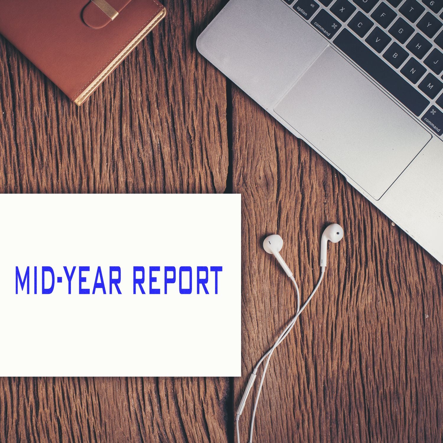 Laptop, earbuds, and mid-year report on rustic wooden desk, business workspace flat lay.