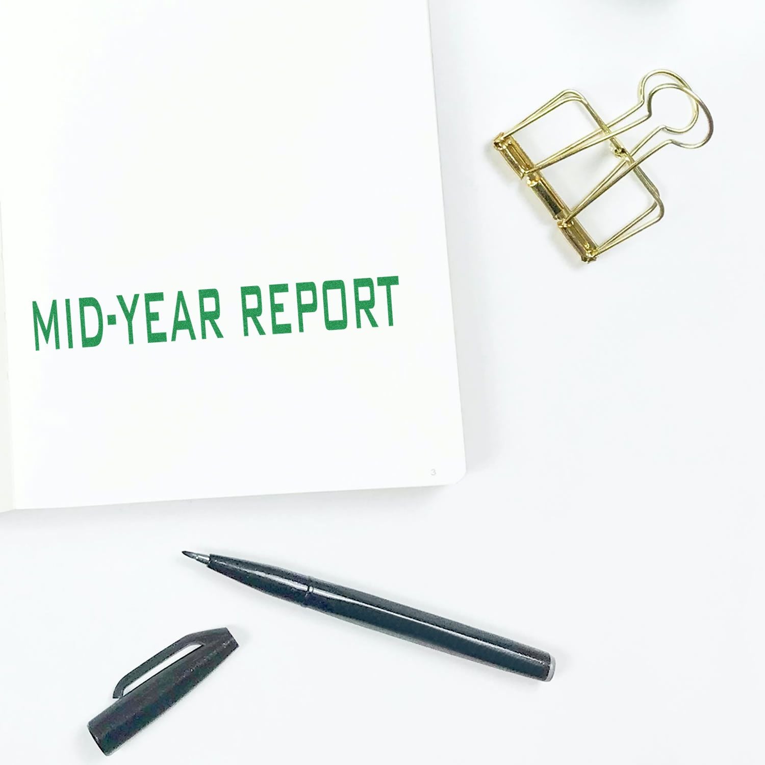 Desk view of a business mid-year report document in white folder with gold paperclip and pen for planning and progress review